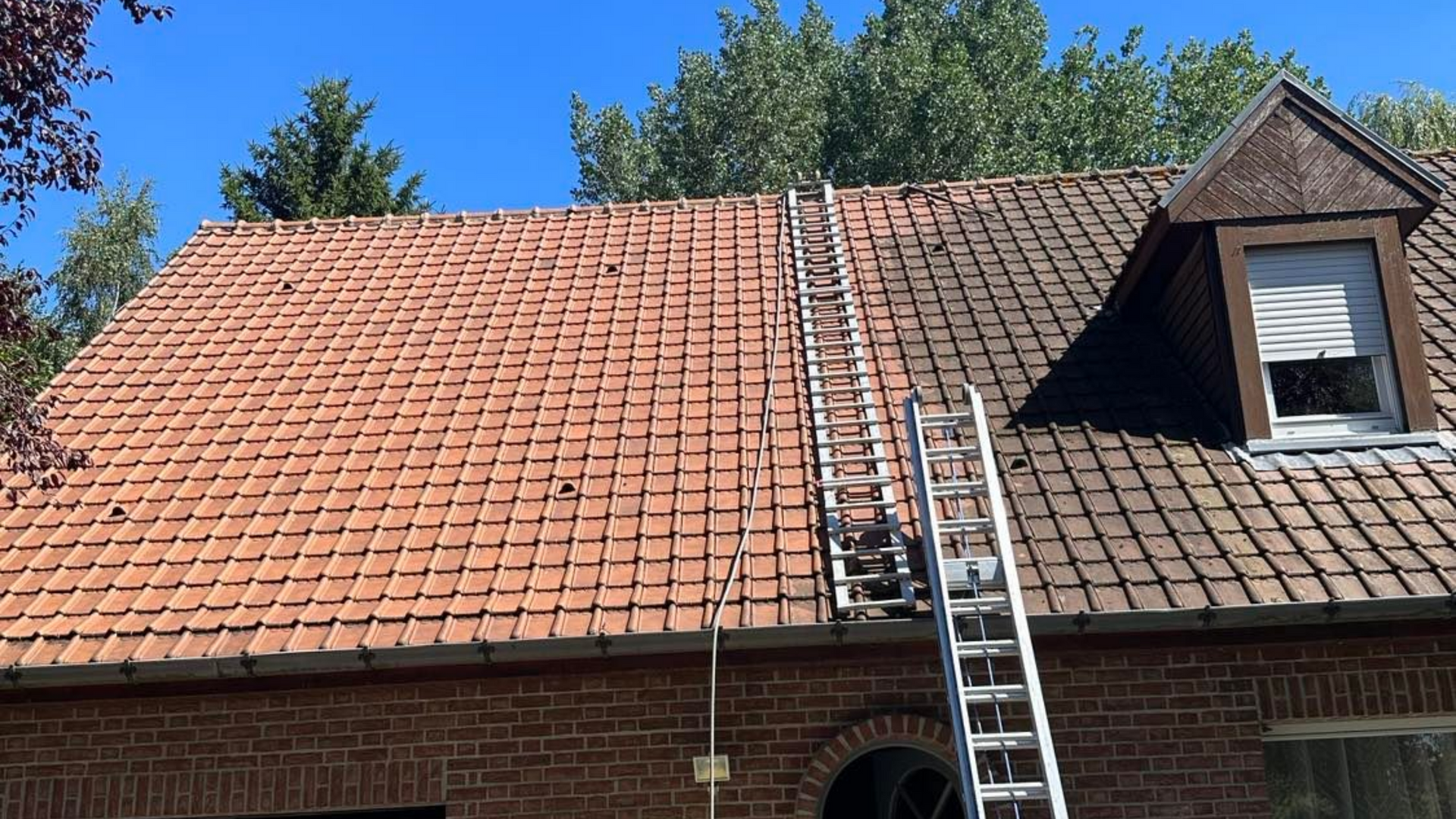 Une personne nettoie au nettoyeur à haute pression un toit de tuiles.