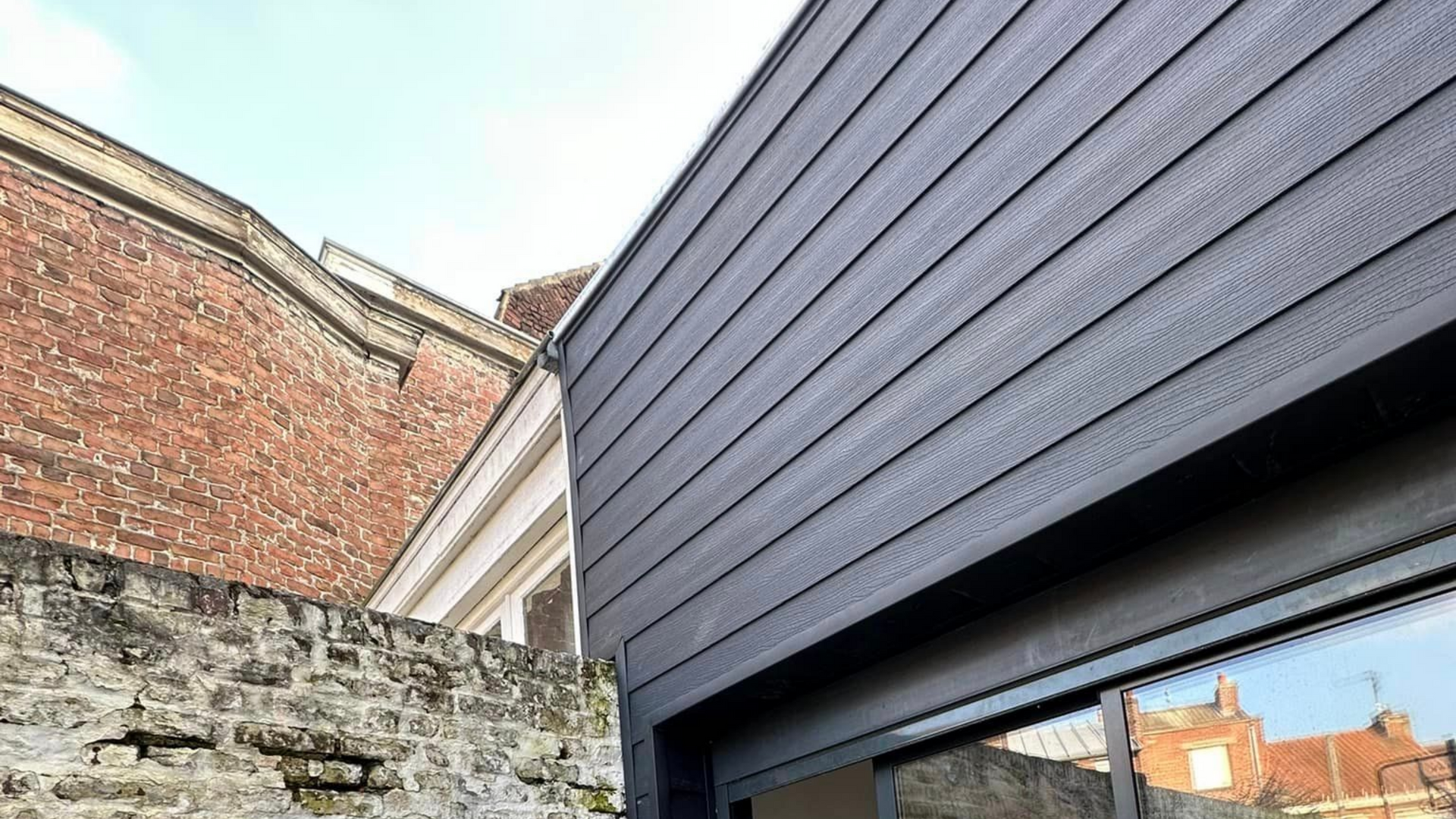 Vue extérieure : bardage en bois gris d’un bâtiment moderne.