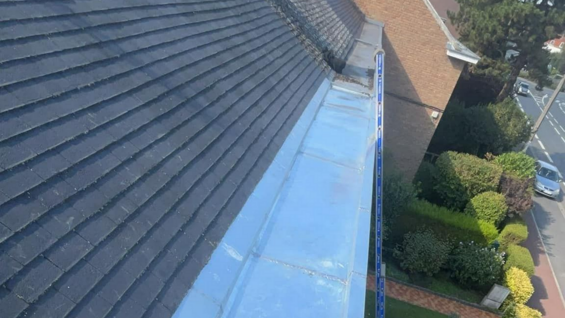 Vue aérienne d'un toit en tuiles rouge avec panneaux solaires, cheminée, puits de lumière.