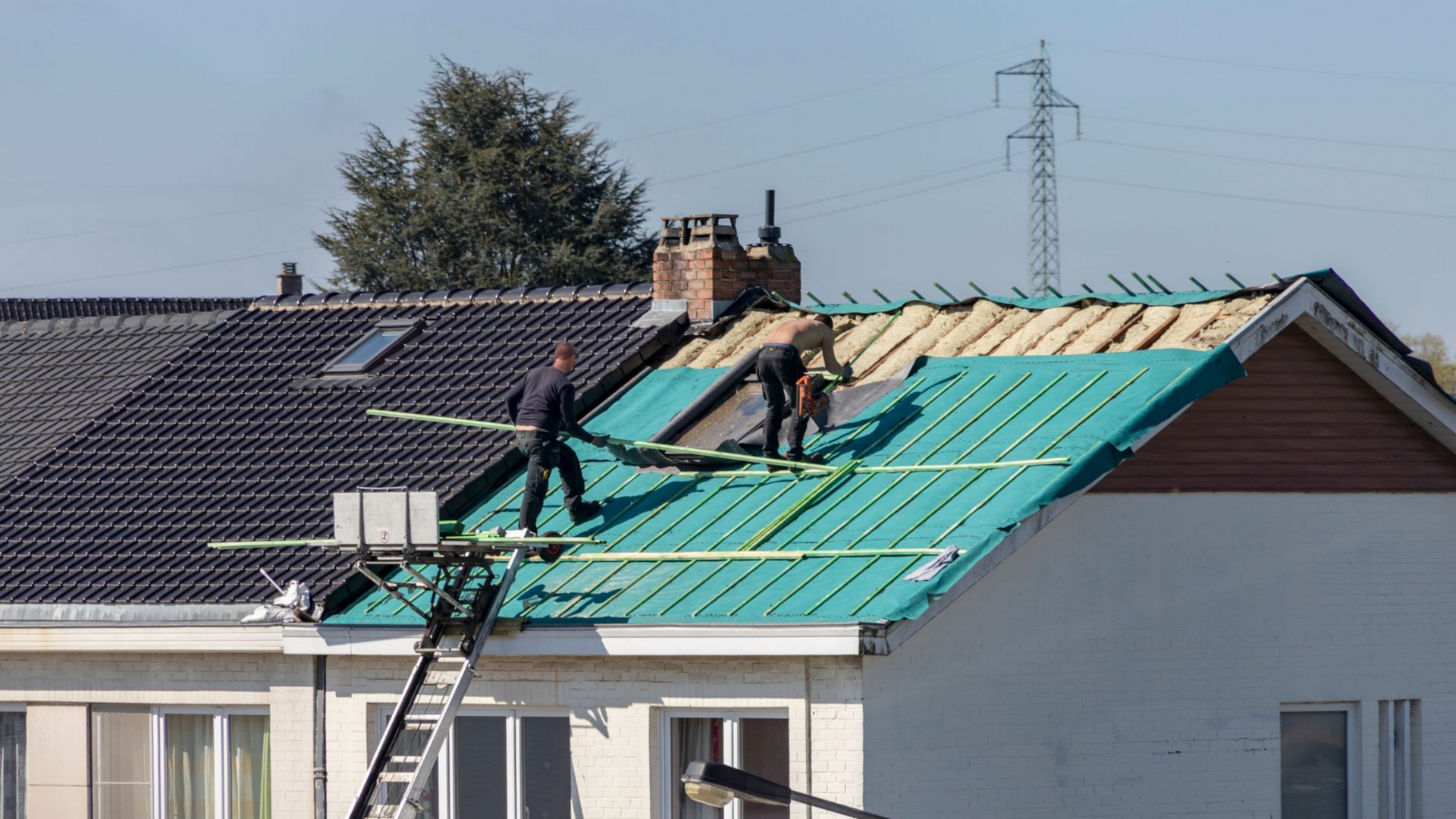 Deux ouvriers sur un toit installent des matériaux de toiture.