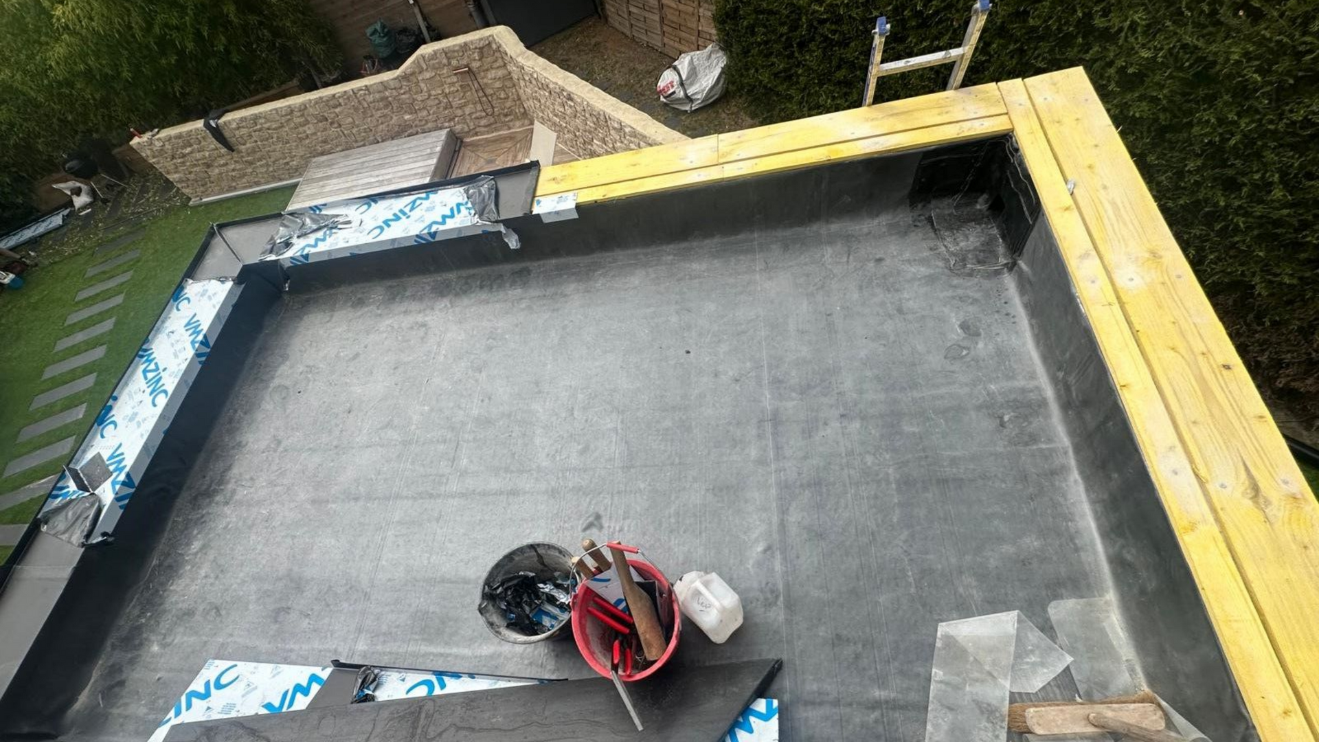 Des mains déroulent un matériau de toiture noir.