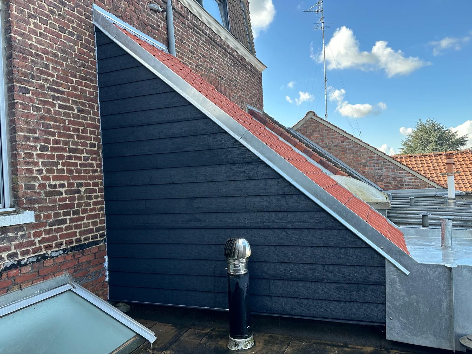 Bardage noir sur un bâtiment aux grandes fenêtres, reflétant l'extérieur.