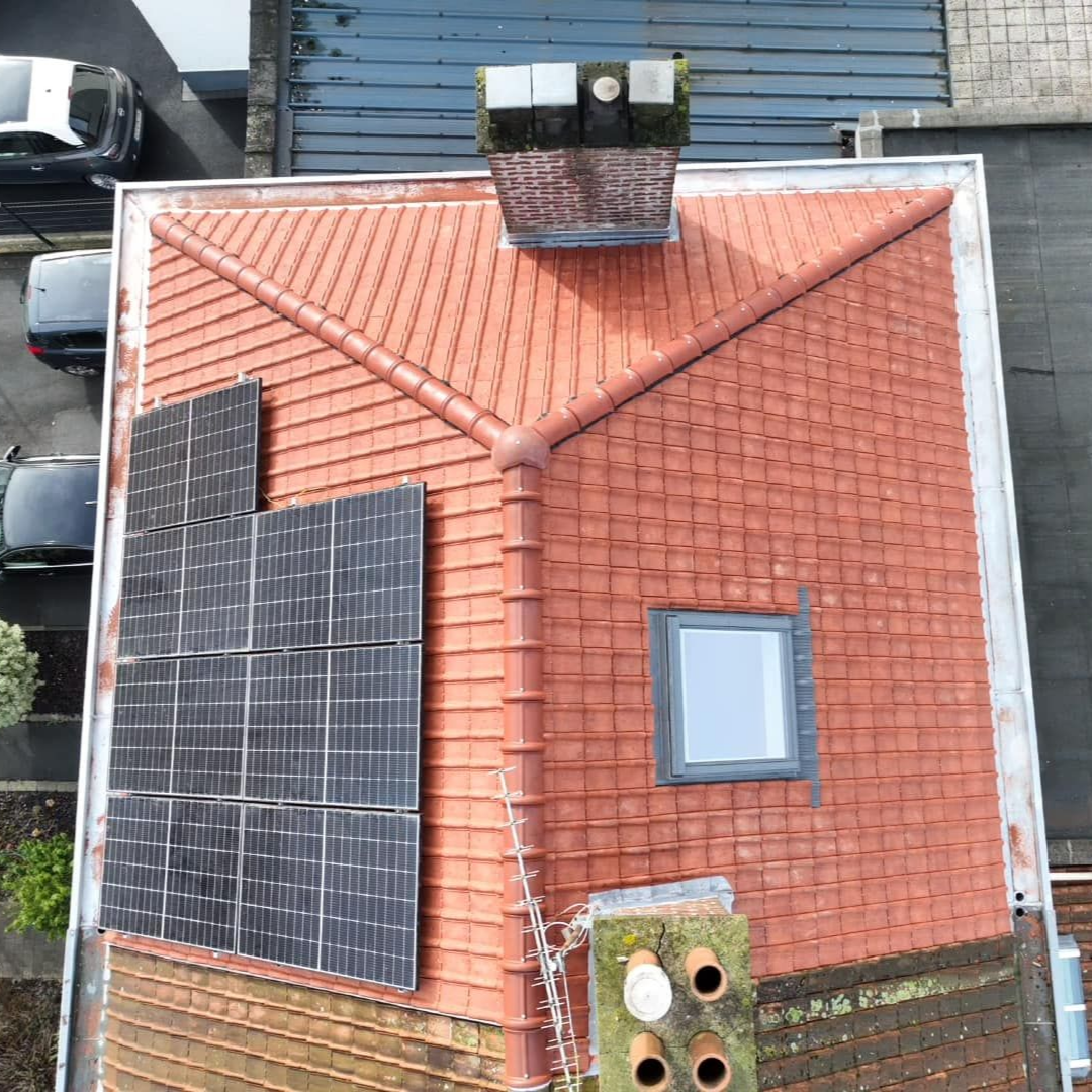 Vue aérienne d'un toit en tuiles rouge avec panneaux solaires, cheminée, puits de lumière.