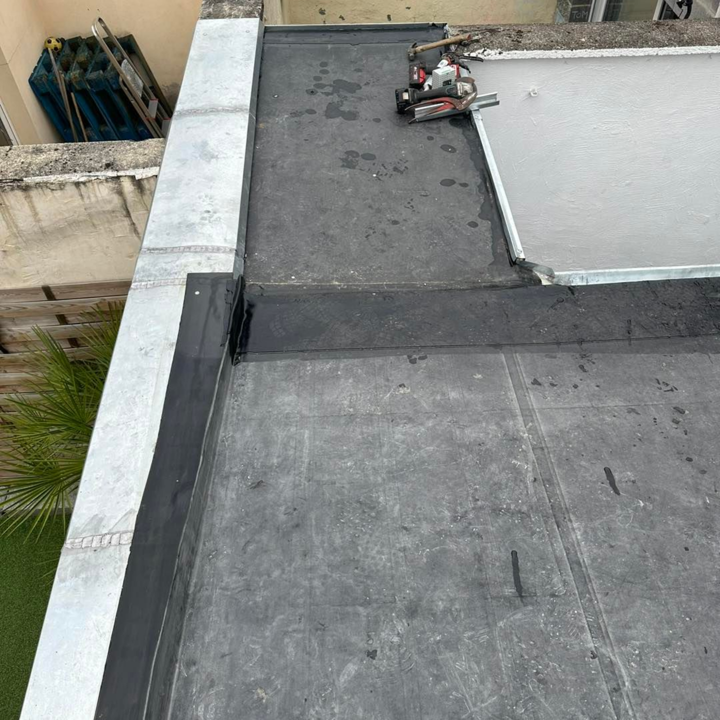 Un toit plat avec une bordure métallique et une section en cours de travail avec des outils.