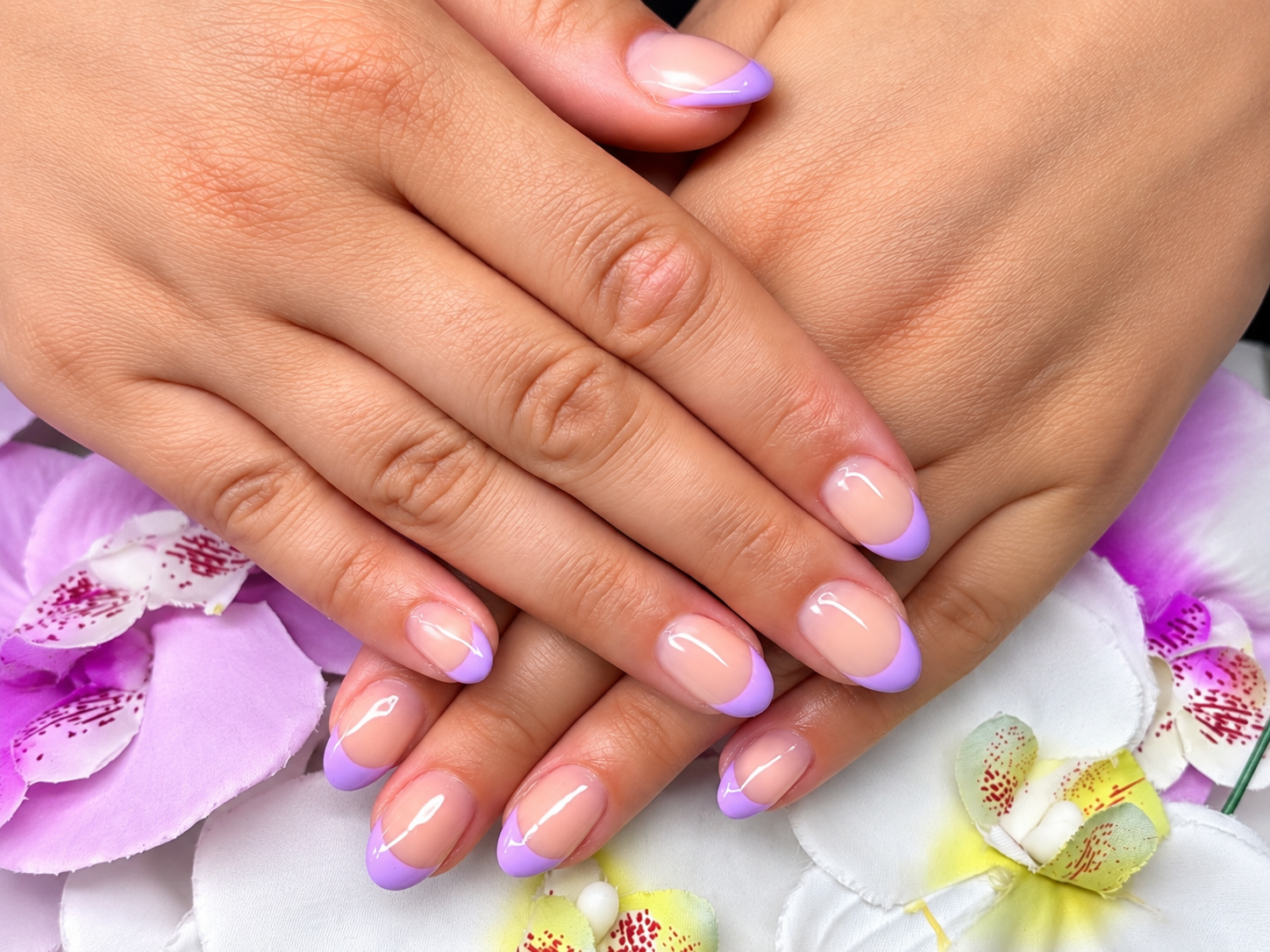 Hände mit lavendelfarbenen Nägeln, die auf weißen und violetten Orchideen ruhen
