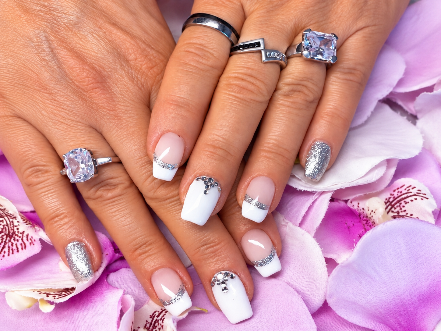 Hände mit lavendel- und weißfarbenem Nagellack und silbernen Ringen über rosa Orchideenblütenblättern
