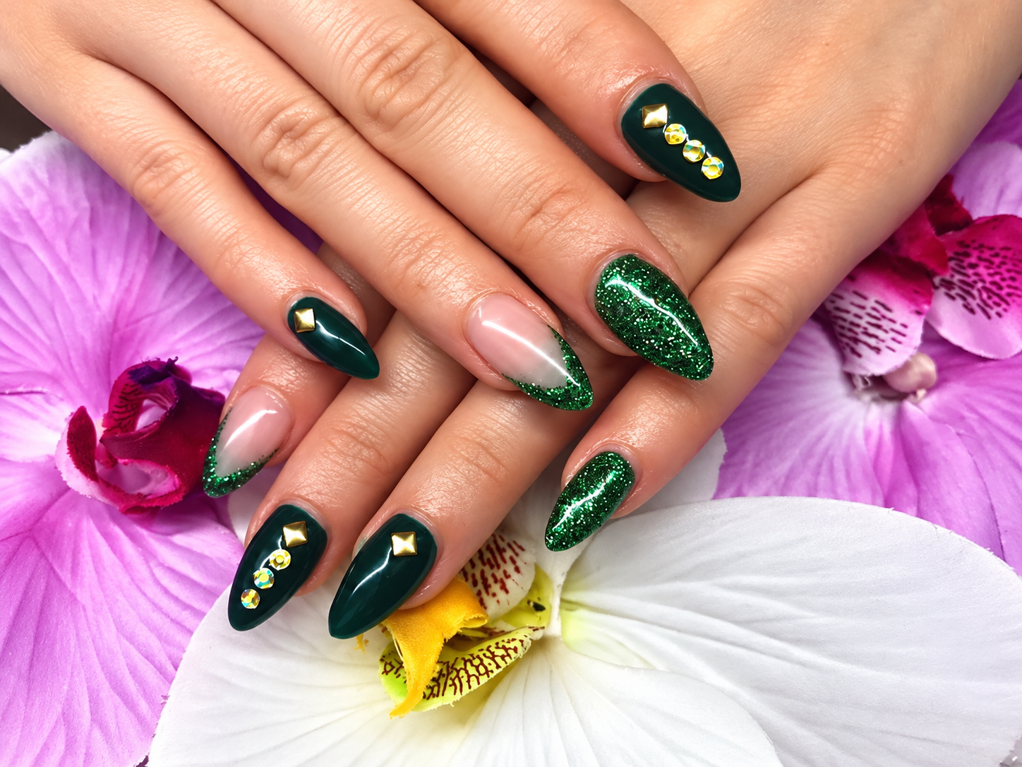 Hände mit dunkelgrünen Glitzernägeln, die auf rosa und weißen Orchideen ruhen.