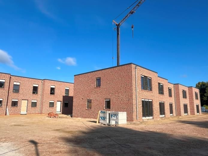 Backstein-Wohnhaus im Bau, Kran, blauer Himmel, Erdboden im Vordergrund