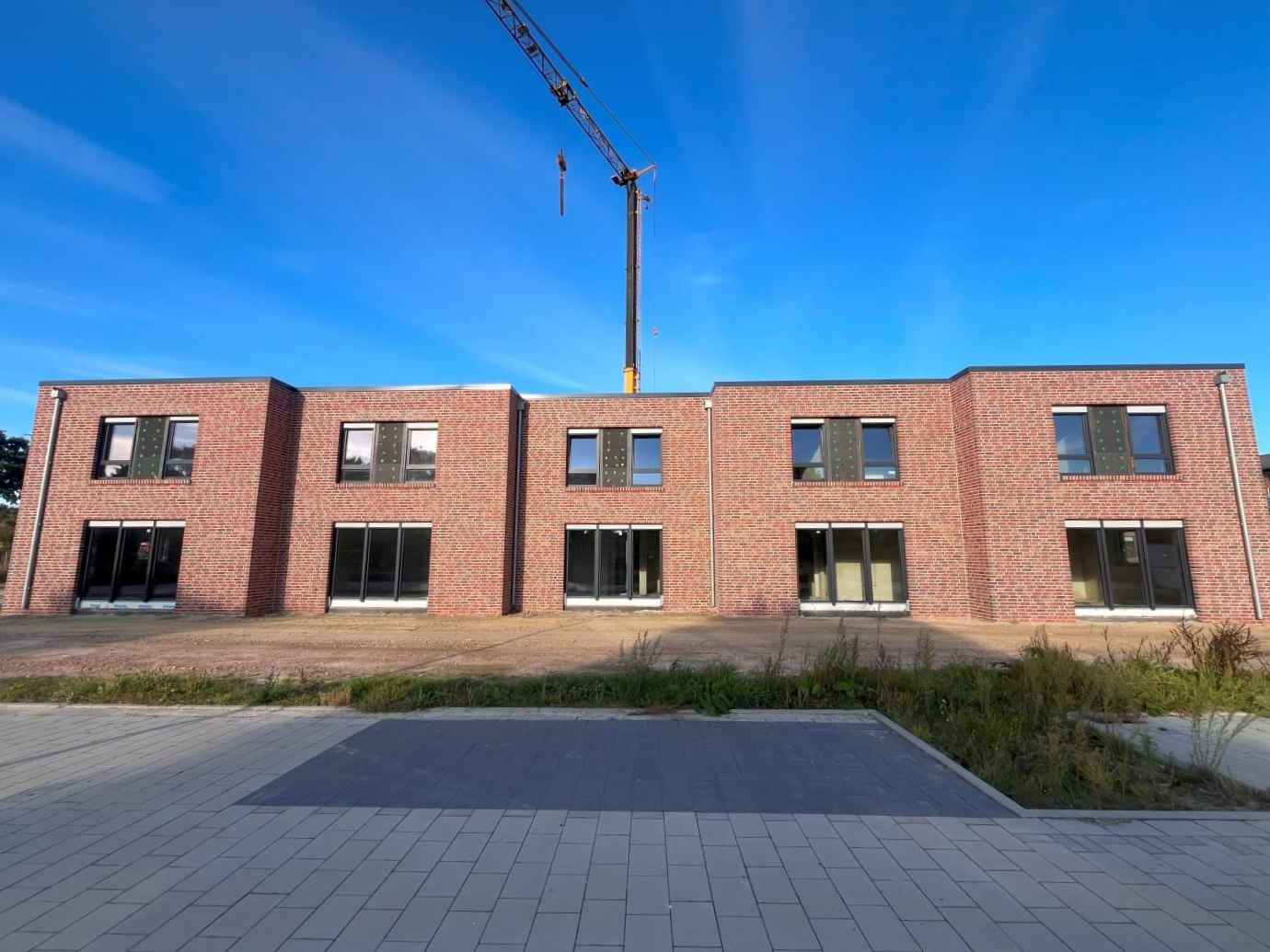 Backstein-Wohnhaus im Bau, darüber ein Kran, davor eine gepflasterte Fläche
