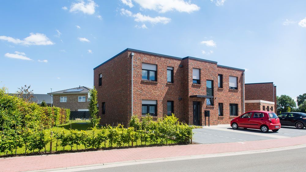 Ein rotes Auto steht vor einem großen Backsteingebäude.