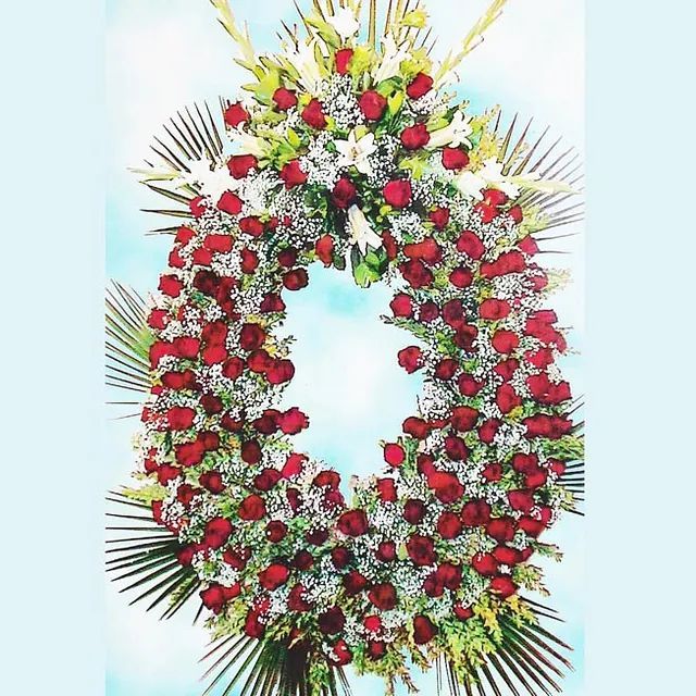 Una corona de rosas rojas y flores blancas sobre un fondo azul.