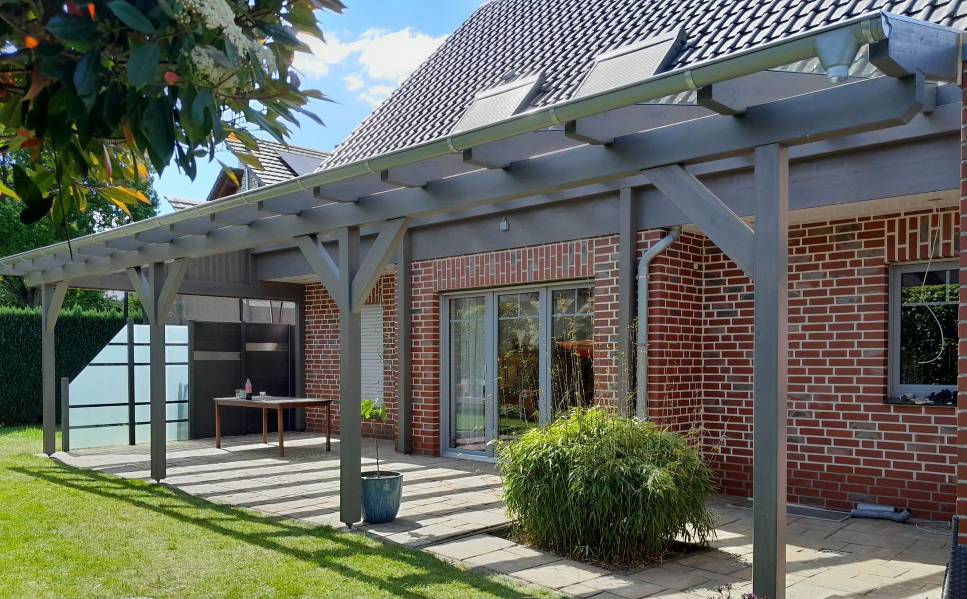 Ein Backsteinhaus mit Pergola und davor liegender Terrasse.