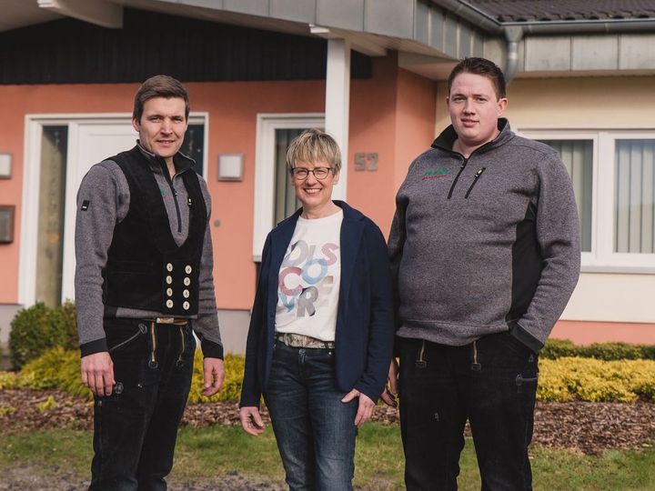 Drei Personen stehen vor einem Haus.