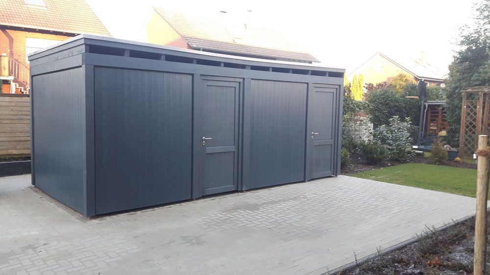 Auf einer gepflasterten Auffahrt in einem Hinterhof steht ein schwarzer Schuppen.