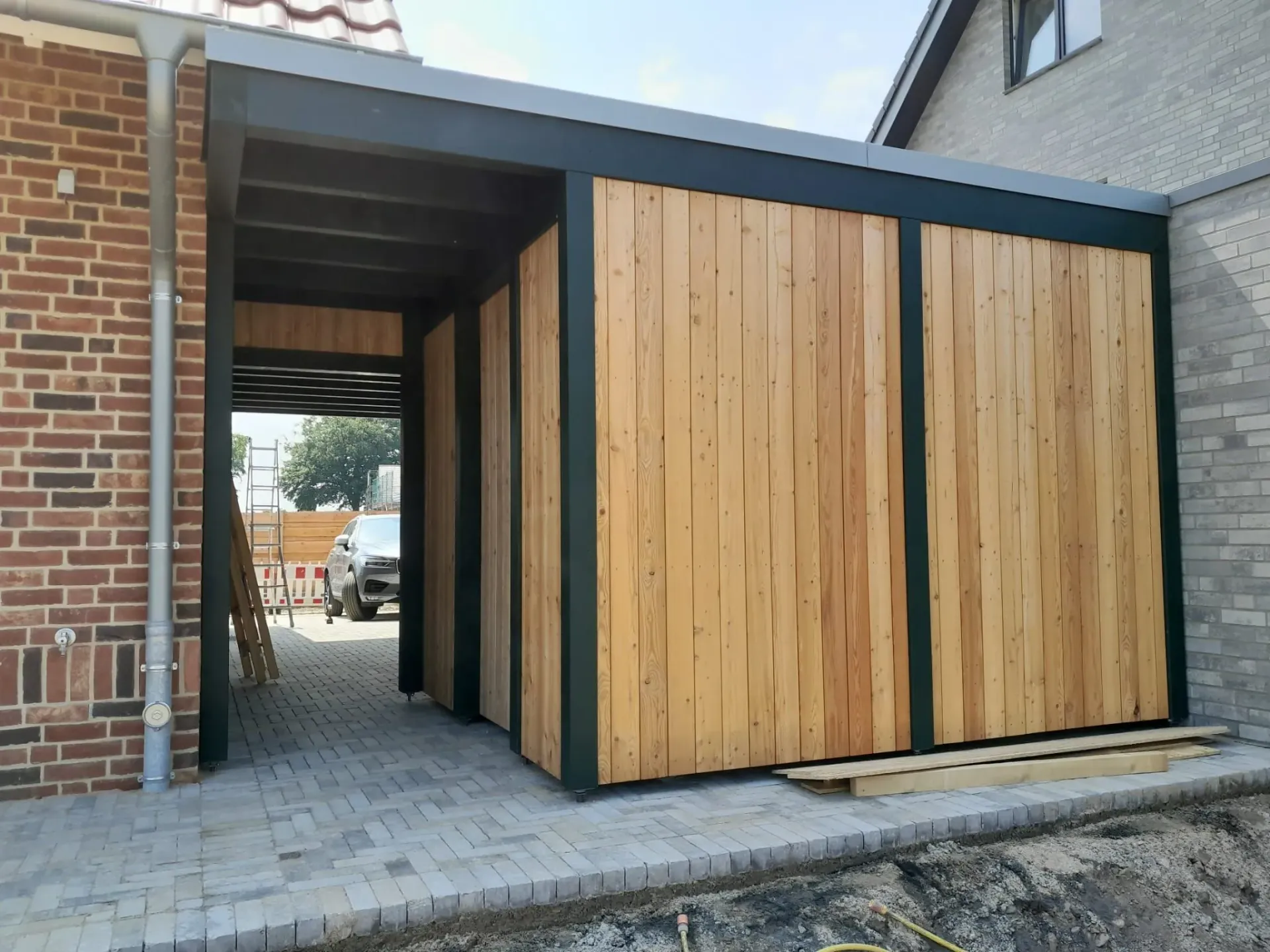Vor einem Backsteingebäude wird eine Holzgarage errichtet.