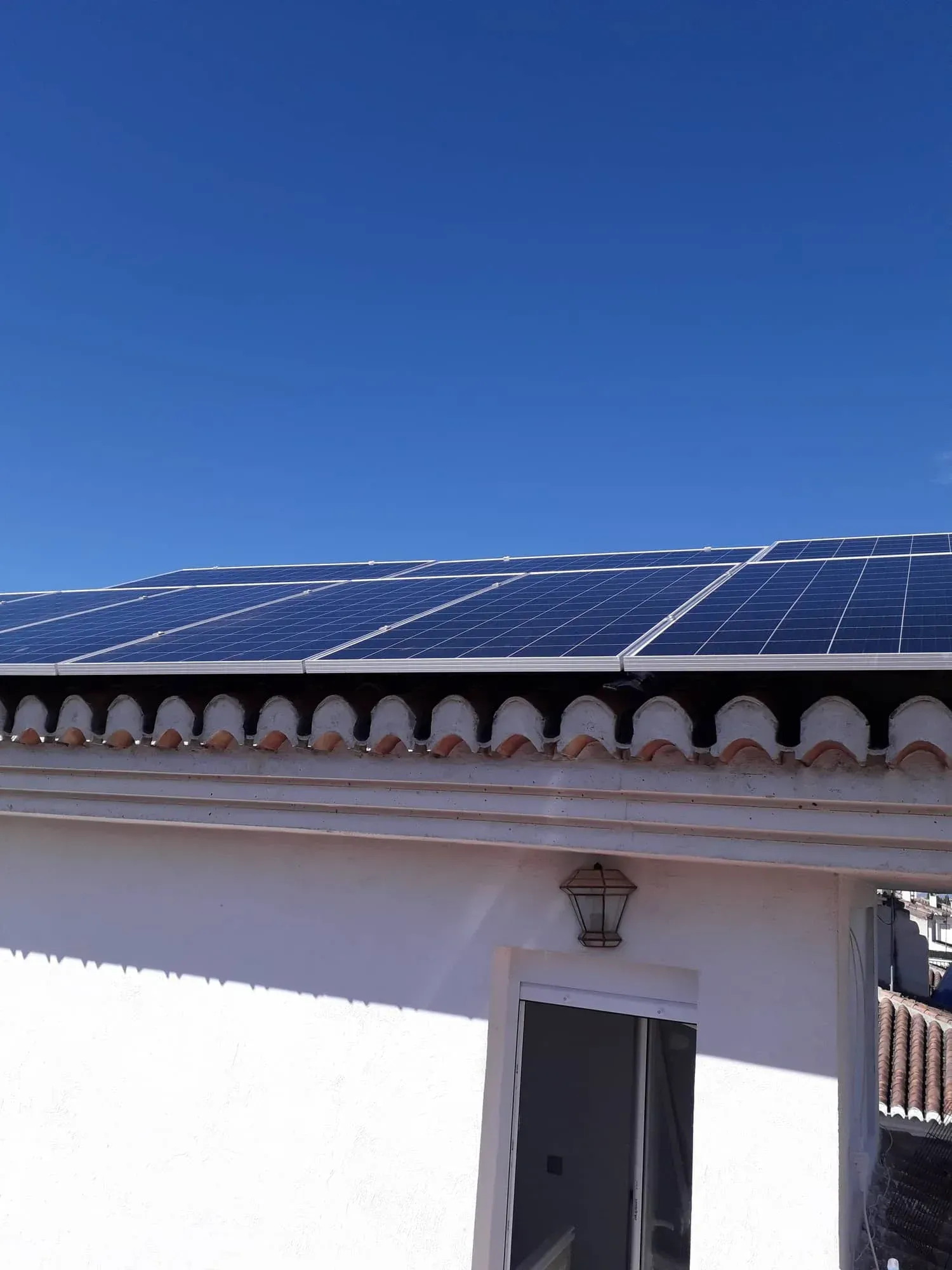 Paneles solares en un tejado contra un cielo azul despejado sobre la entrada de un edificio blanco.