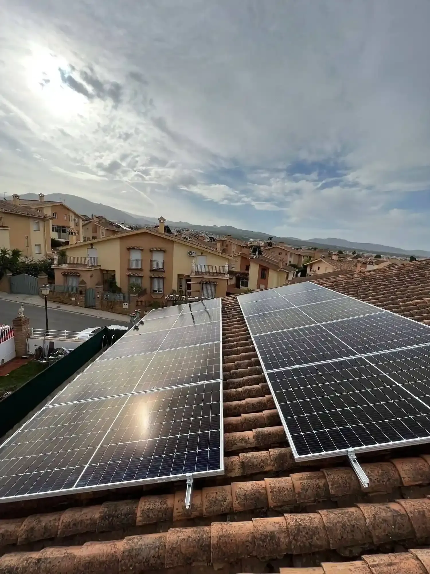 Paneles solares en un tejado de tejas con vistas a un barrio residencial nublado.