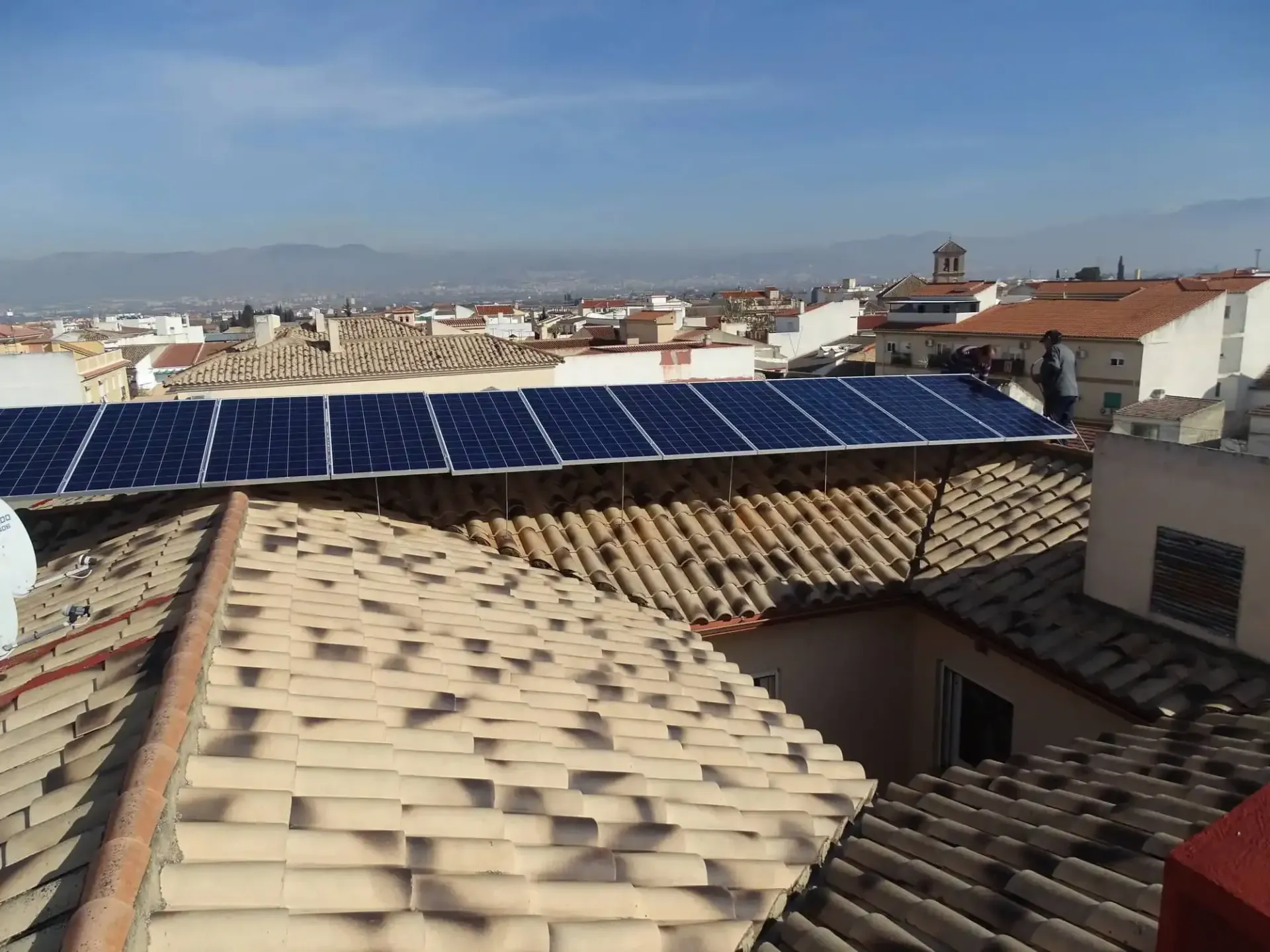 Paneles solares en los tejados de tejas con vistas al horizonte de la ciudad bajo un cielo despejado.