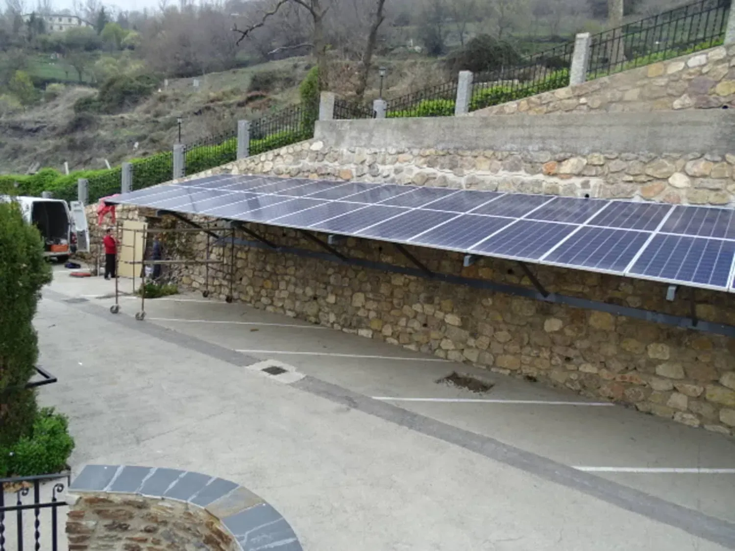 Edificio de piedra con paneles solares a lo largo de un sendero inclinado, rodeado por una ladera y árboles.