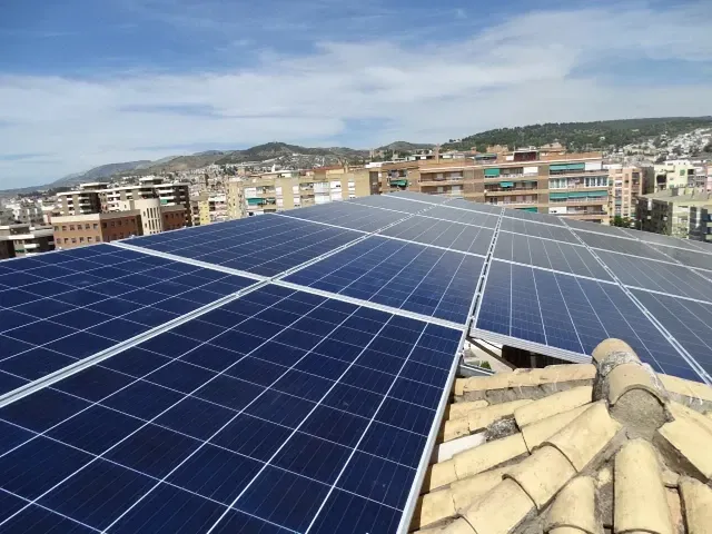 Paneles solares en una azotea con un paisaje urbano y colinas al fondo.