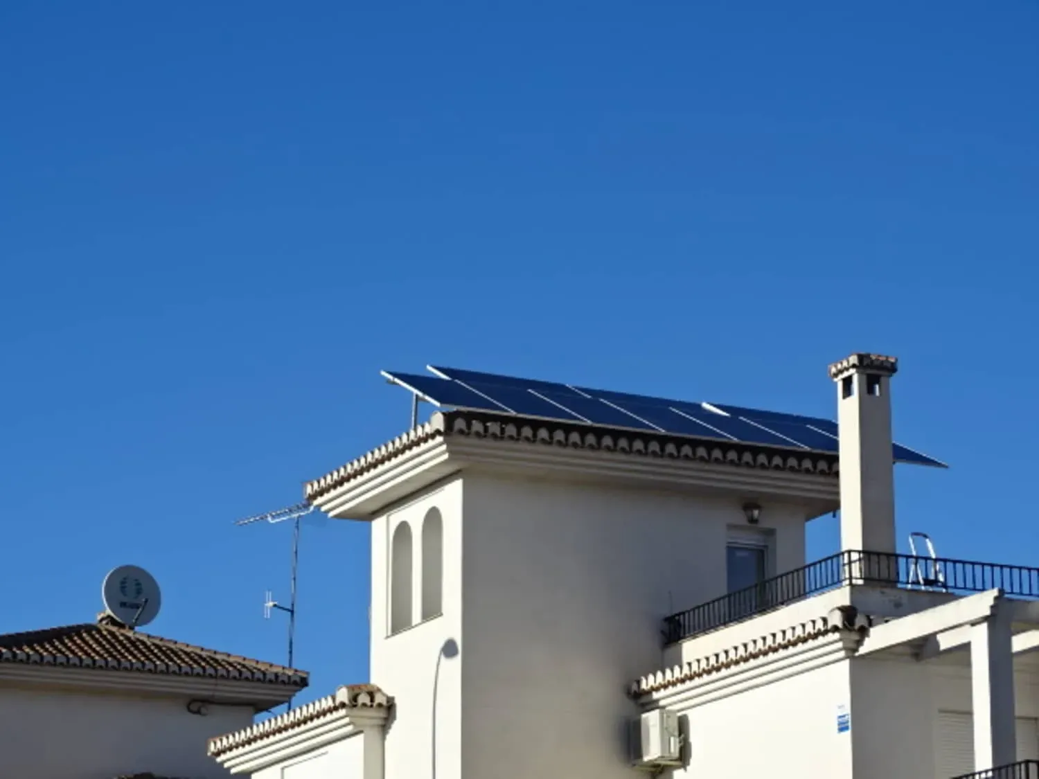 Casas blancas de estilo mediterráneo con tejados de tejas y chimeneas bajo un cielo azul claro.
