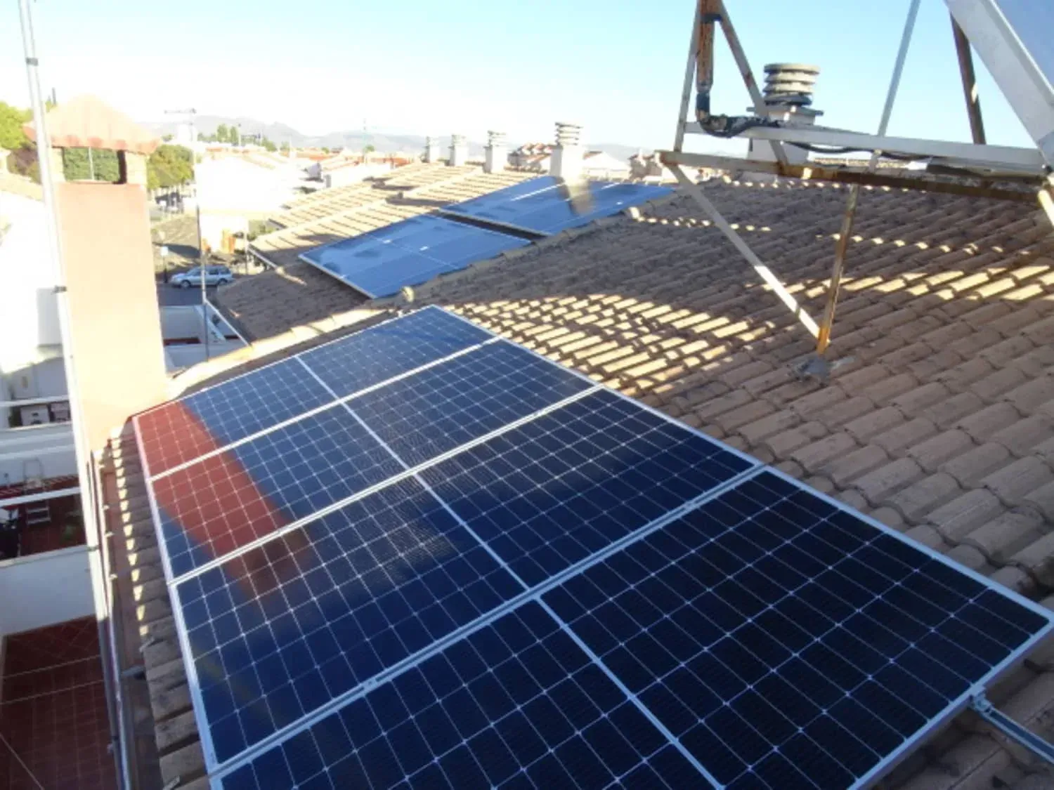 Paneles solares instalados en un tejado de tejas bajo la brillante luz del sol, con edificios de la ciudad al fondo.