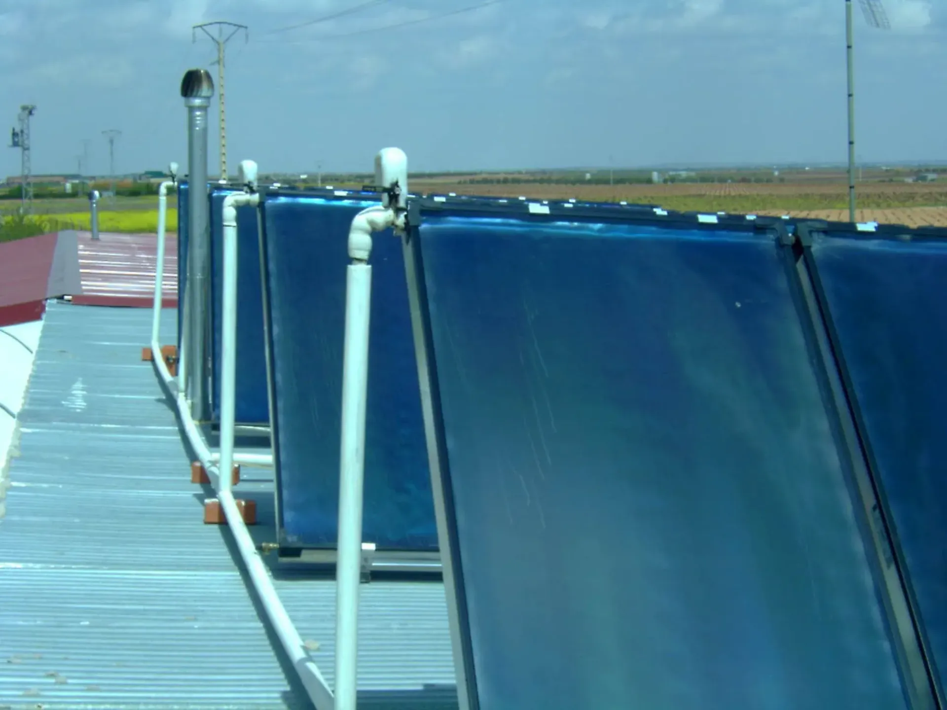 Paneles solares térmicos azules en un tejado con tuberías metálicas y el cielo del desierto al fondo.