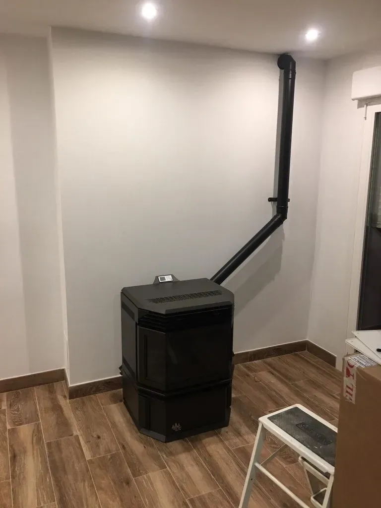 Estufa de pellets negra con tubo de ventilación negro en una habitación pequeña
