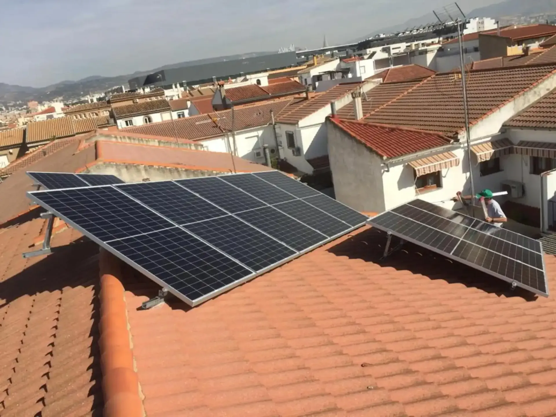 Paneles solares instalados en un tejado de tejas rojas en un barrio residencial, a plena luz del día.