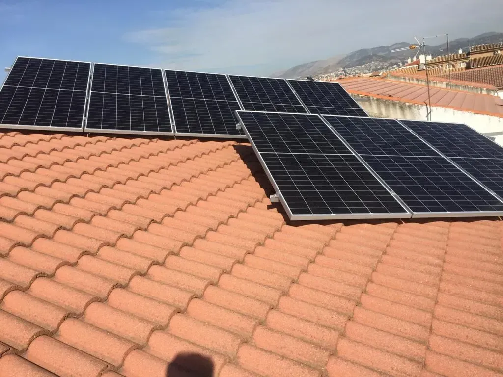 Paneles solares instalados en un tejado de tejas de terracota bajo un cielo despejado.