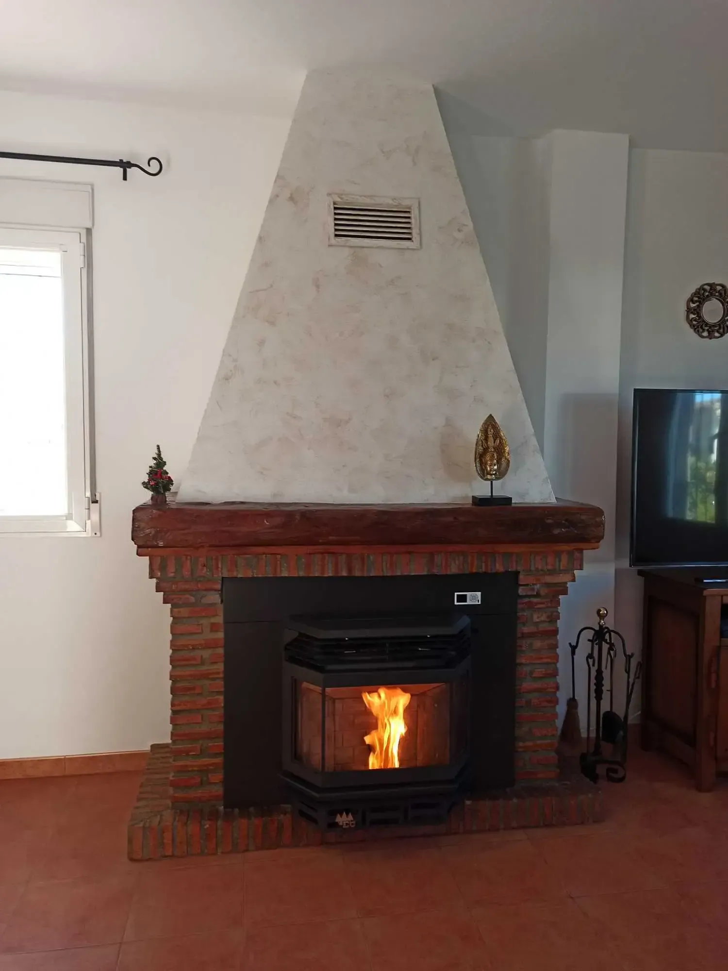 Chimenea de ladrillo con estufa de leña encendida y chimenea blanca en una sala de estar.