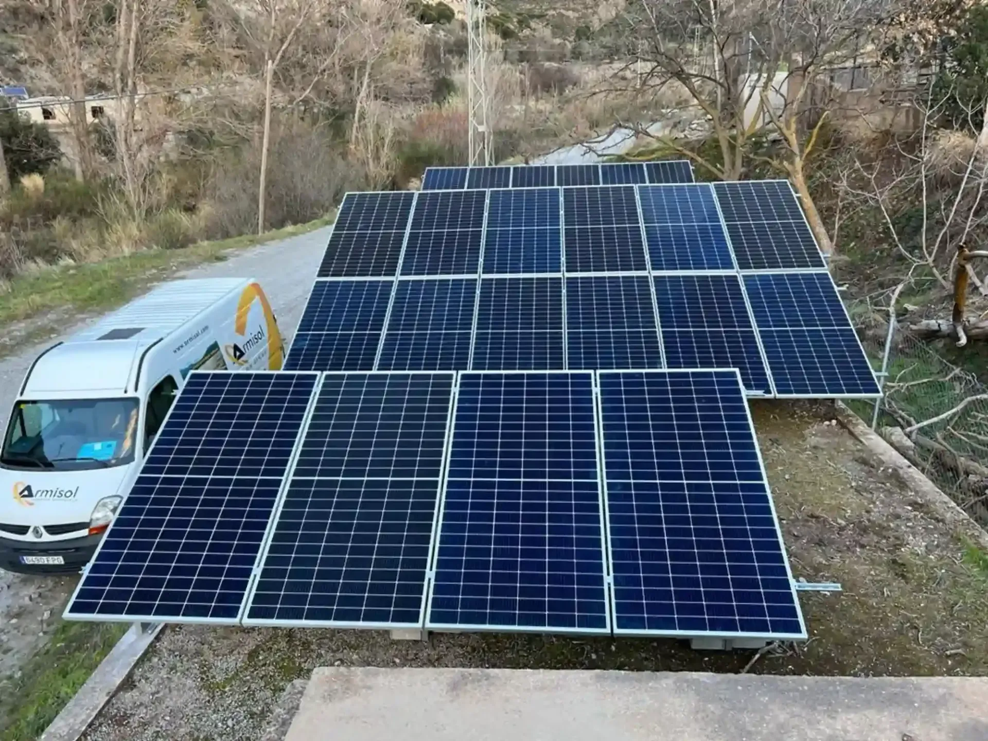 Paneles solares azules instalados en una furgoneta blanca en una zona rural con árboles y colinas.