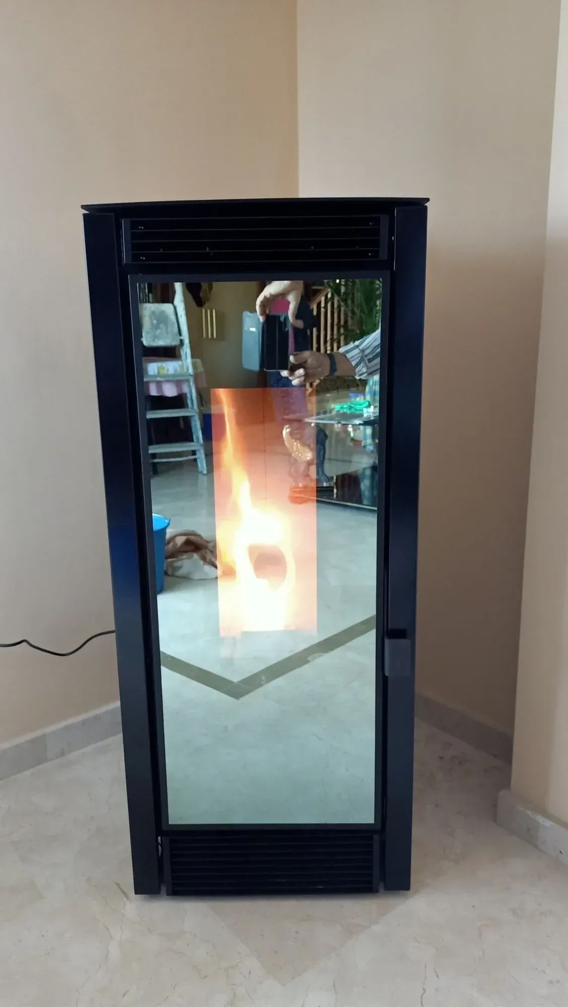 Vitrina con marco negro, puerta con espejo y luz brillante en el interior, ubicada en un pasillo.