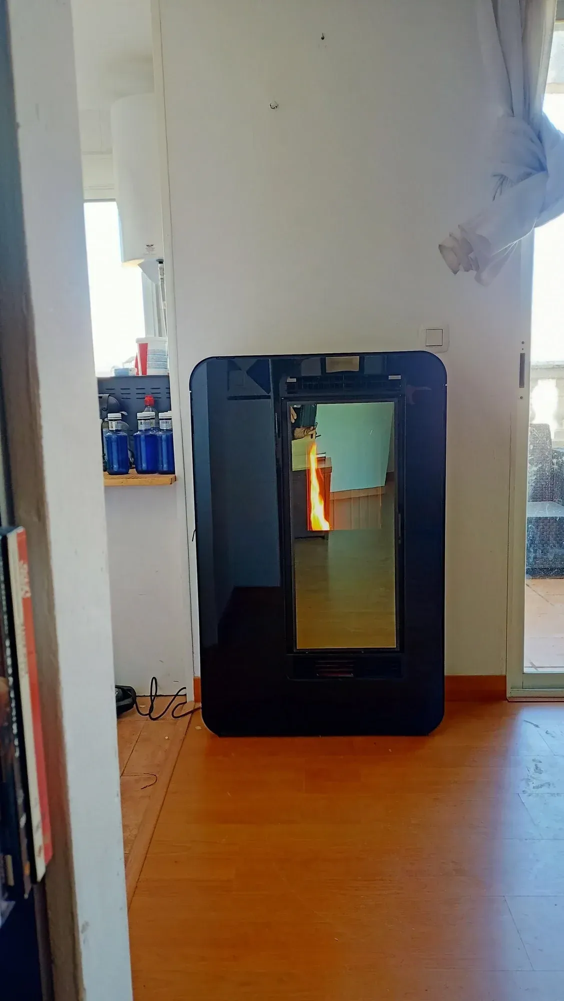 Electrodoméstico negro con forma de mueble y puerta de cristal, colocado contra una pared blanca en una habitación.