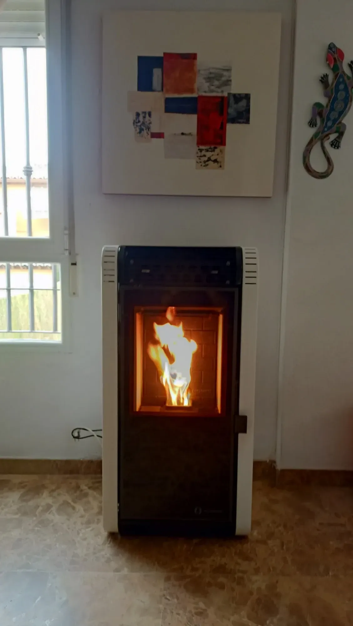 Chimenea o estufa encendida en una habitación luminosa con una obra de arte abstracto en la pared encima.