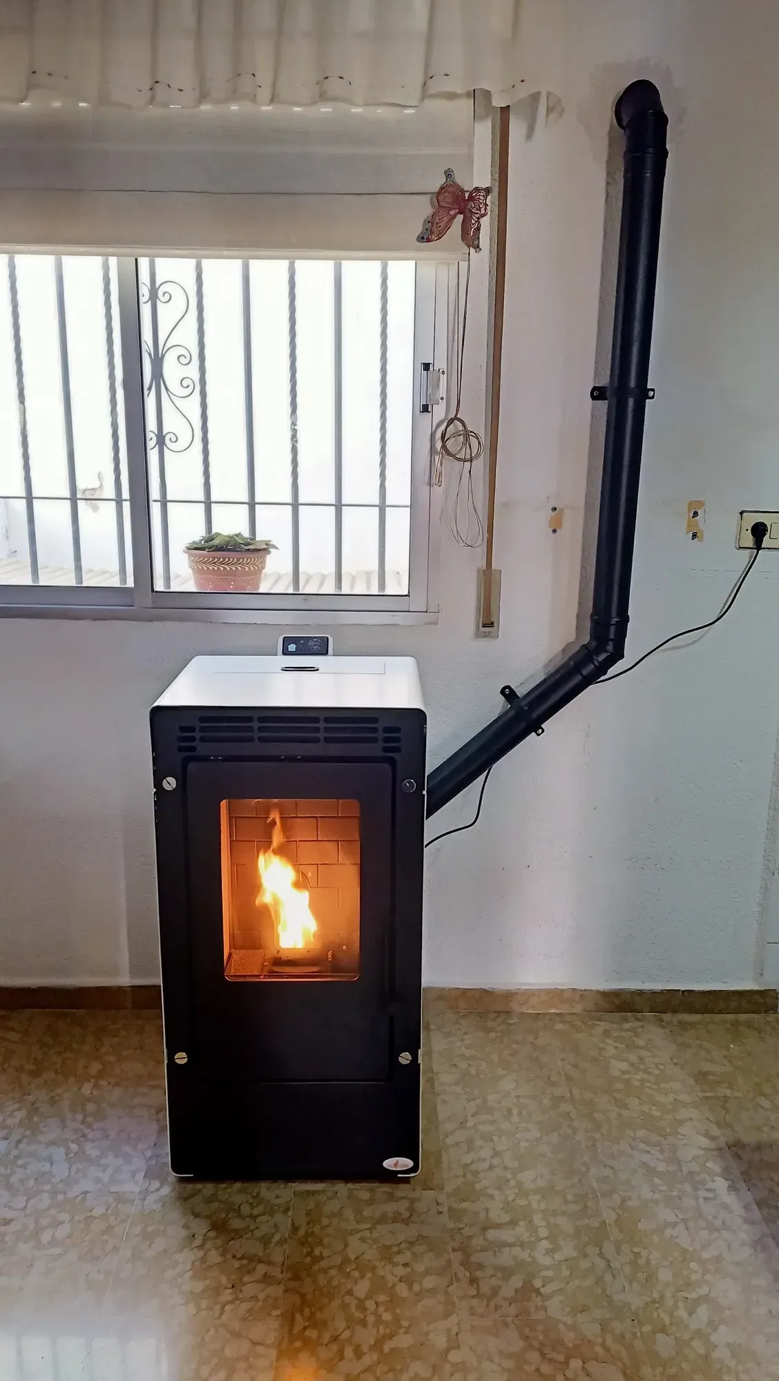 Estufa de pellets negra encendida en una habitación alicatada debajo de una ventana