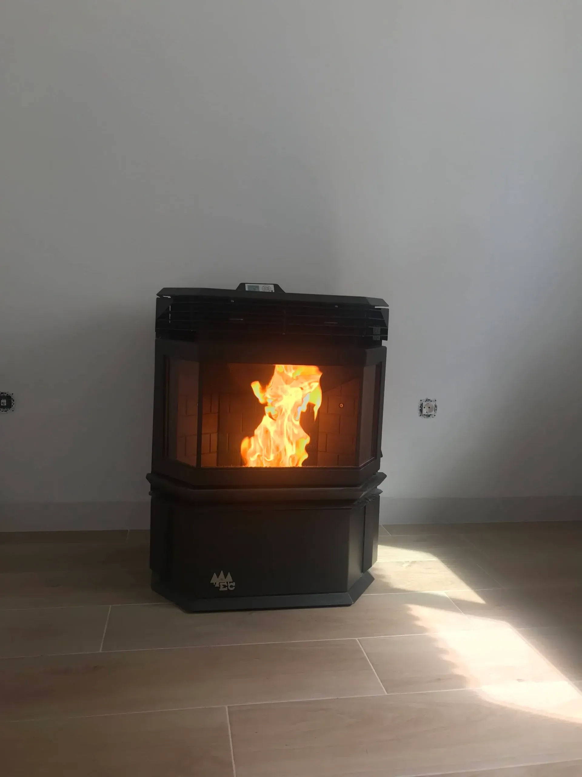 Estufa de leña negra con un fuego brillante ardiendo en su interior en una habitación austera con luz solar en el suelo.