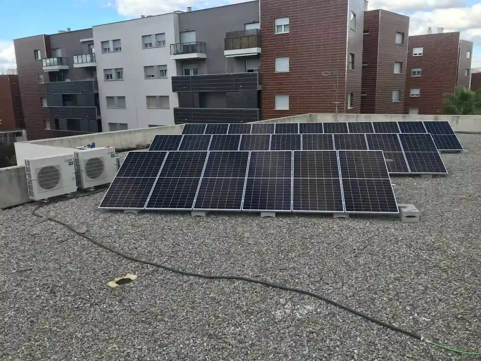 Paneles solares instalados en un tejado de grava con edificios de apartamentos al fondo.