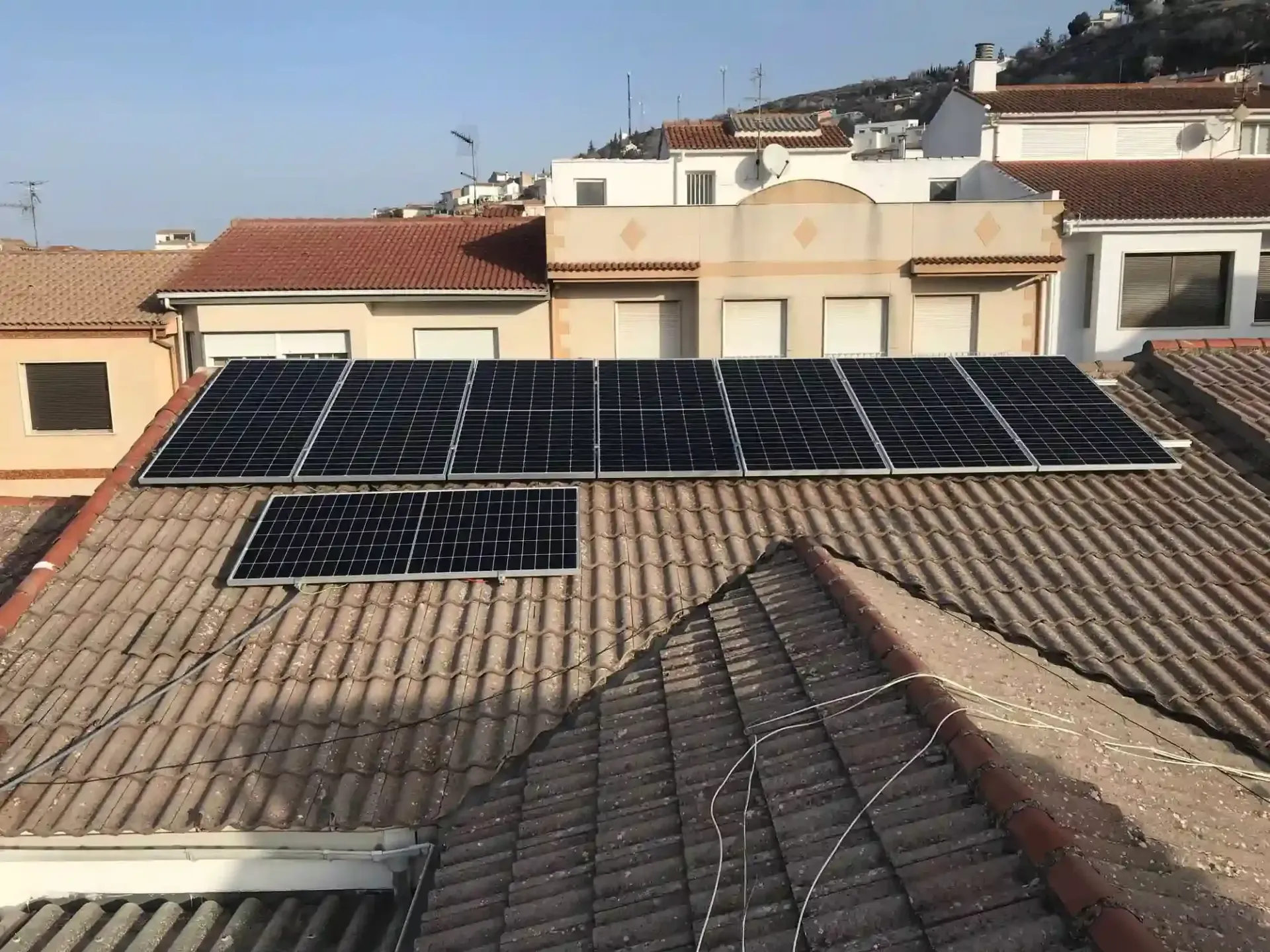Paneles solares instalados en un tejado de tejas en un barrio residencial soleado.