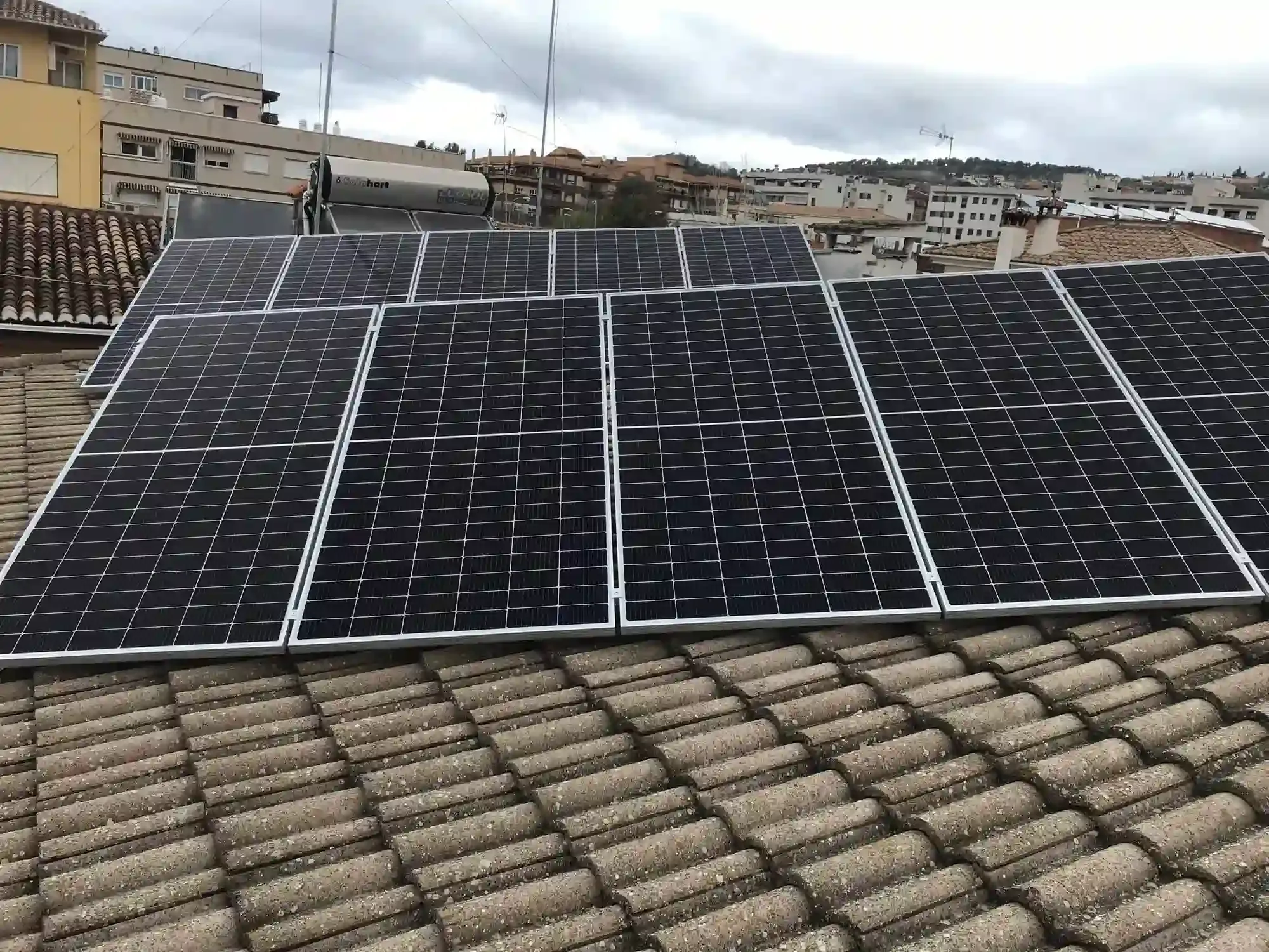 Paneles solares instalados en un tejado de tejas en un paisaje urbano.