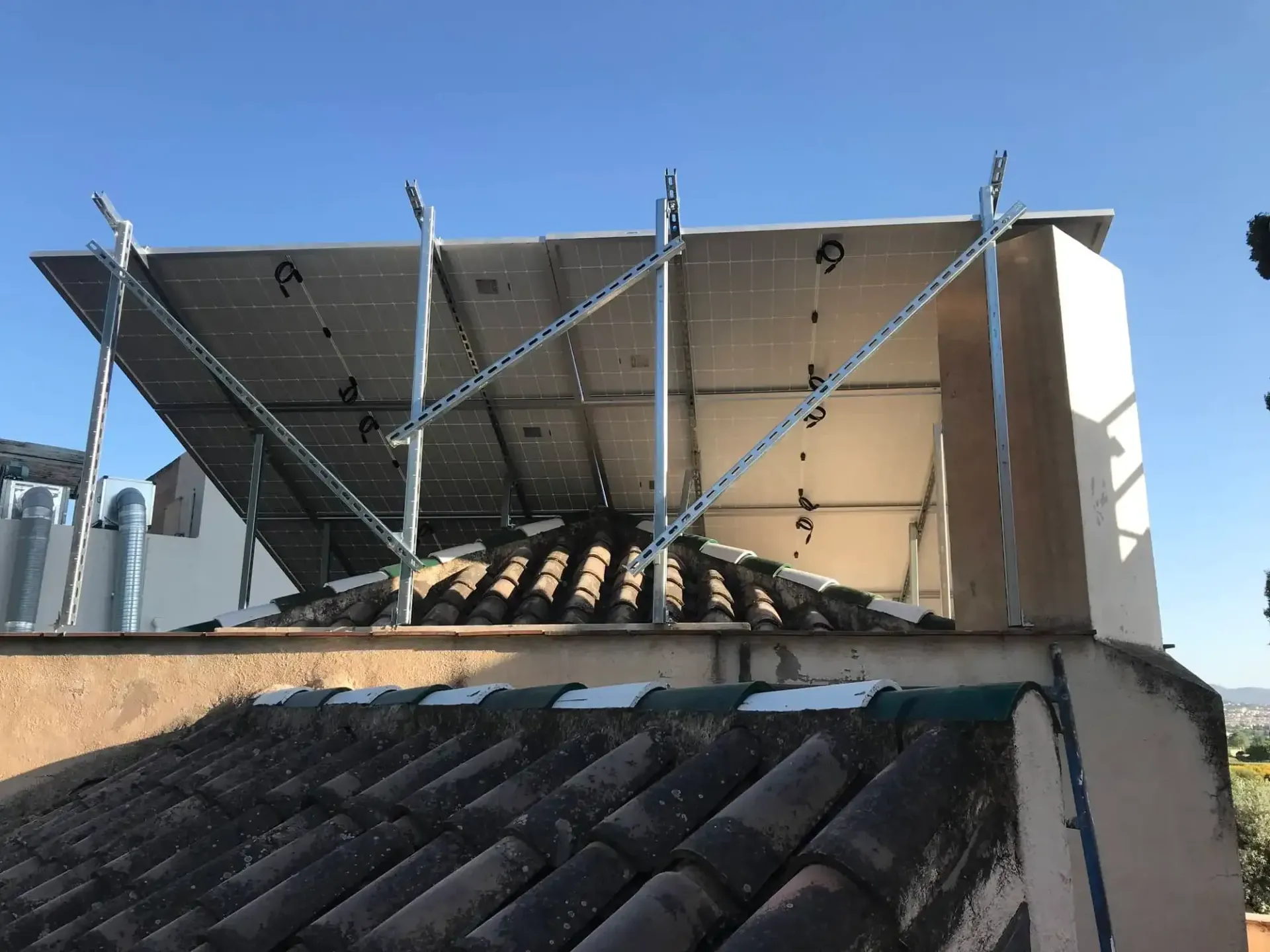 Instalación de paneles solares en la azotea con soportes metálicos y techo ondulado bajo un cielo azul despejado.