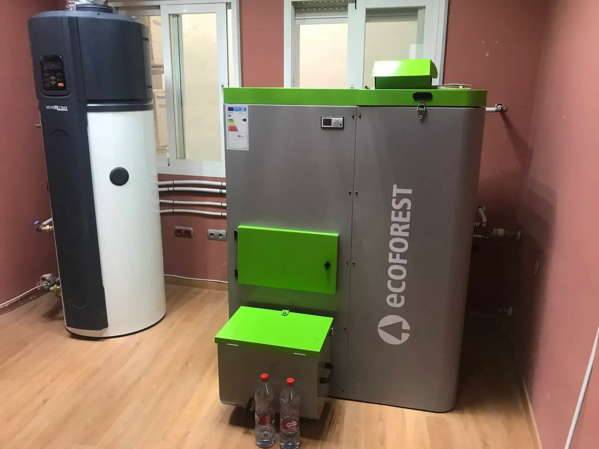 Equipamiento industrial en una habitación: una unidad Ecoforest gris y verde junto a un tanque blanco alto.