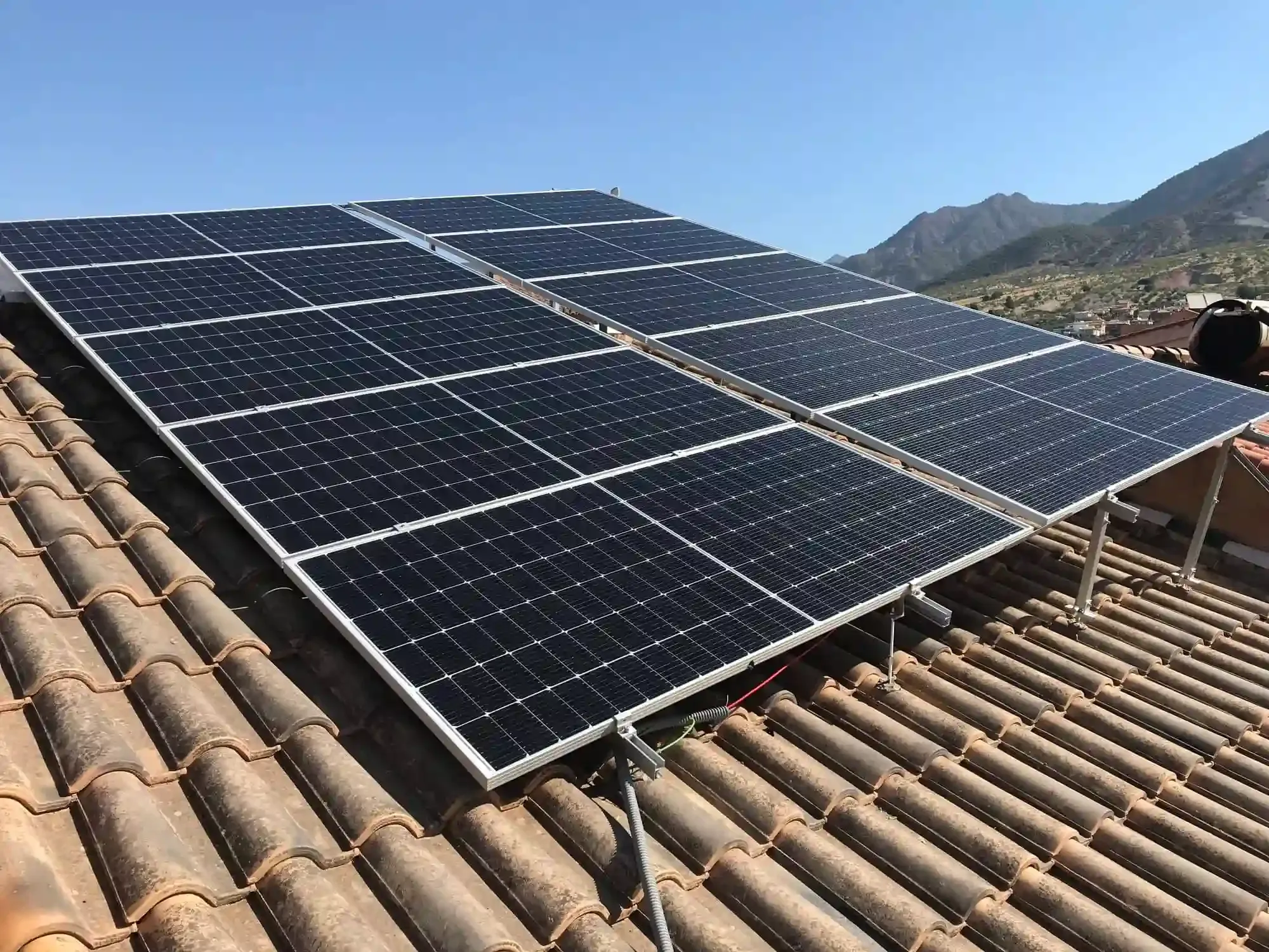 Paneles solares instalados en un tejado de tejas con montañas al fondo.