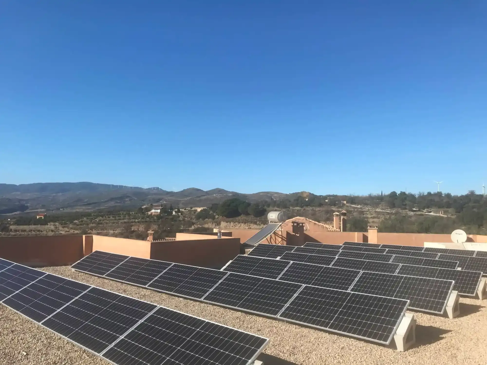 Paneles solares en un tejado con montañas y un cielo azul despejado al fondo.
