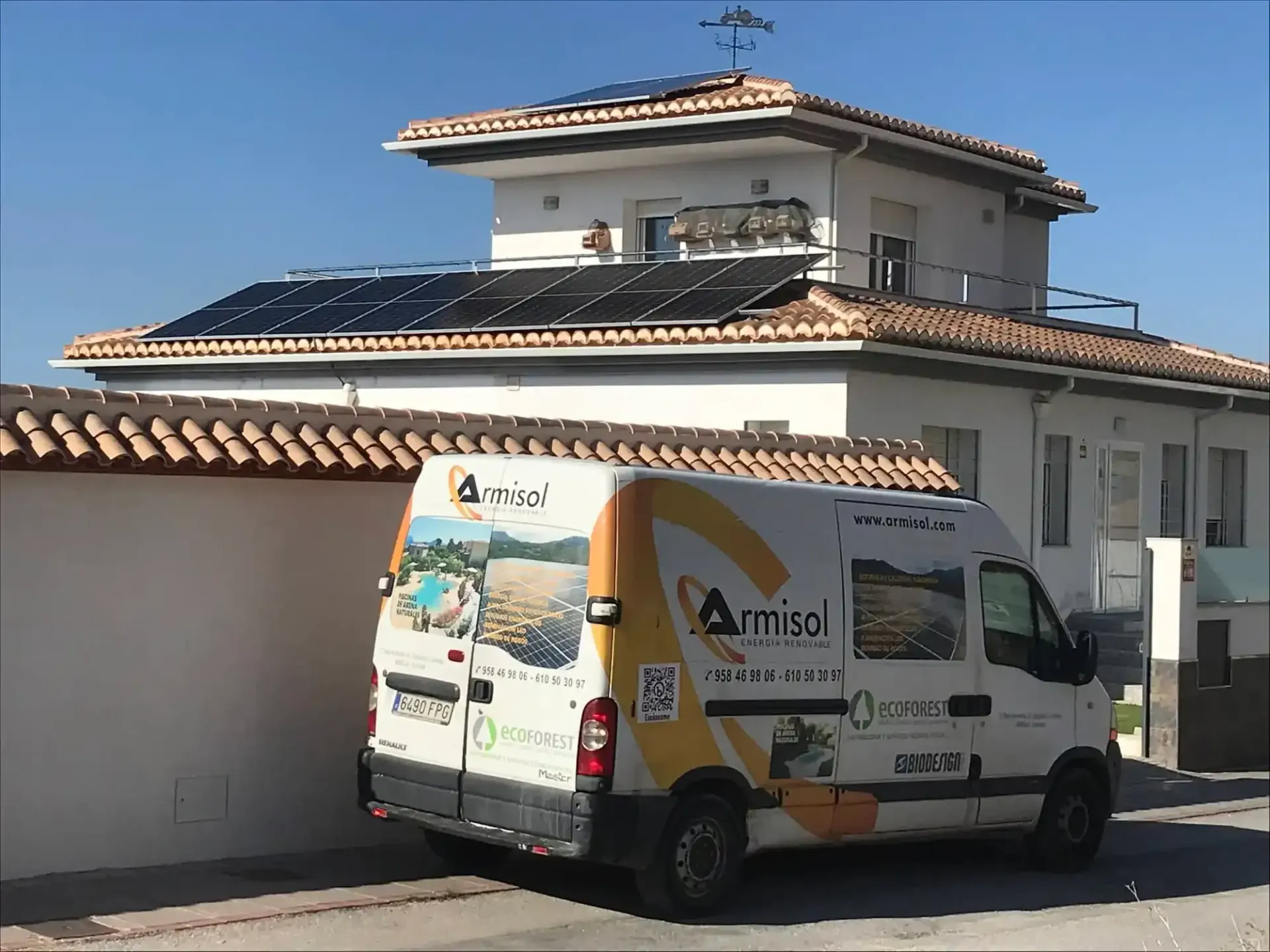 Furgoneta de servicio blanca aparcada frente a una gran casa blanca con tejado de tejas y garaje.
