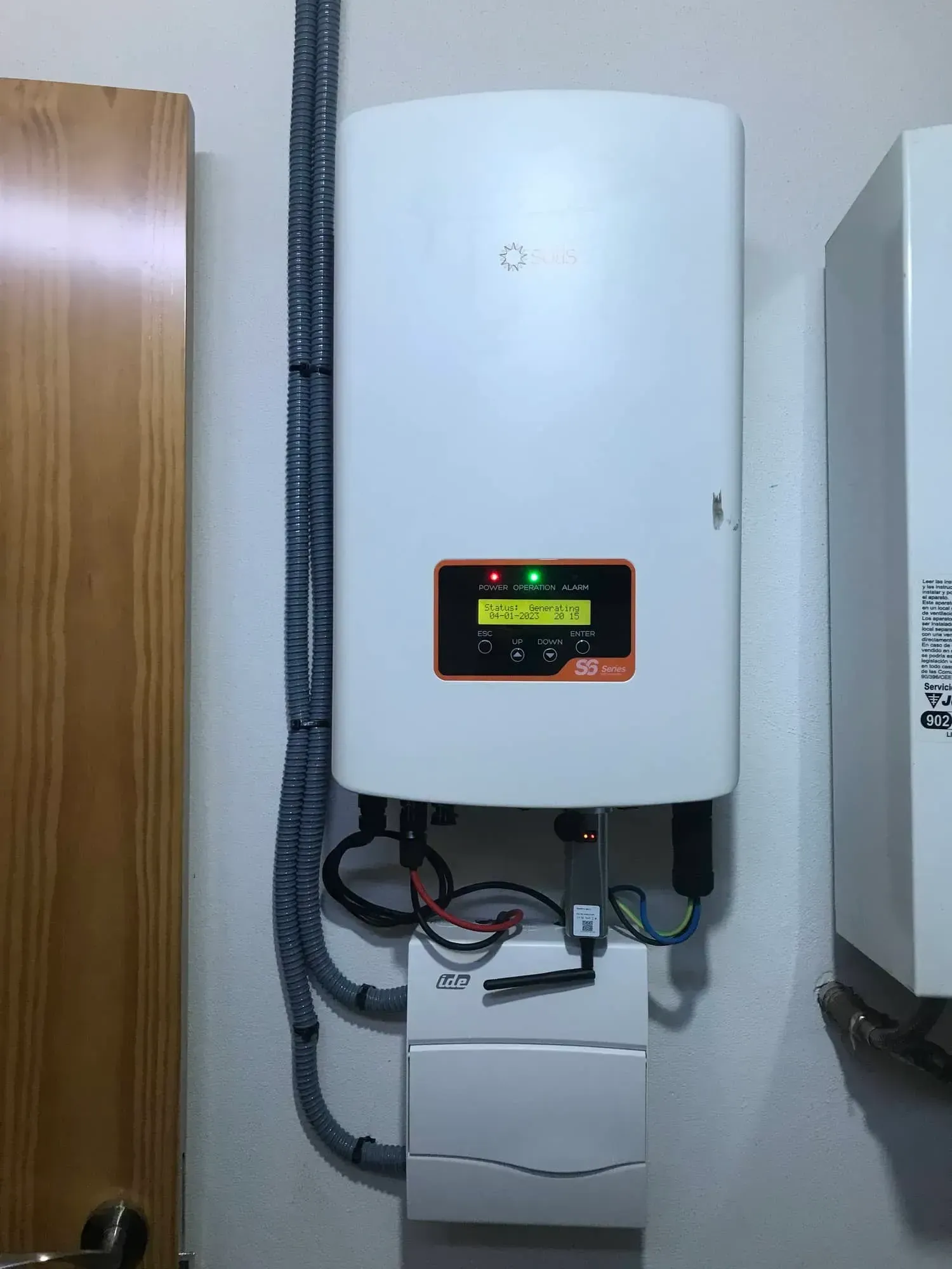 Calentador de agua eléctrico blanco de pared con pantalla digital, tuberías y caja de control en un cuarto de servicio.