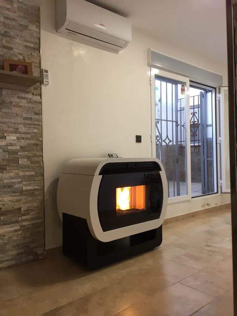 Sala de estar moderna con estufa independiente encendida, suelo de baldosas beige y puerta corrediza de vidrio.
