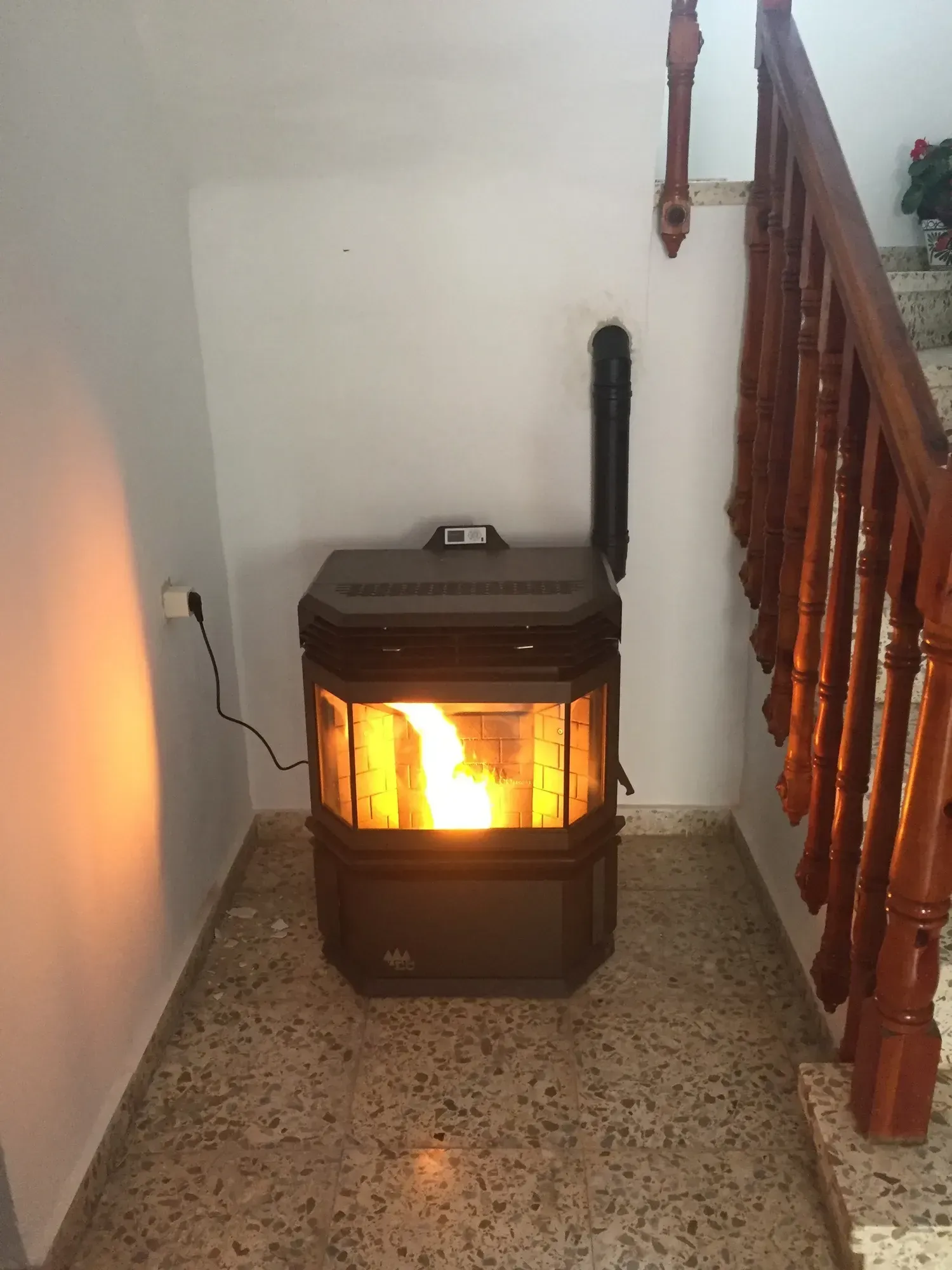 Una estufa de leña encendida ilumina un pasillo junto a una escalera.