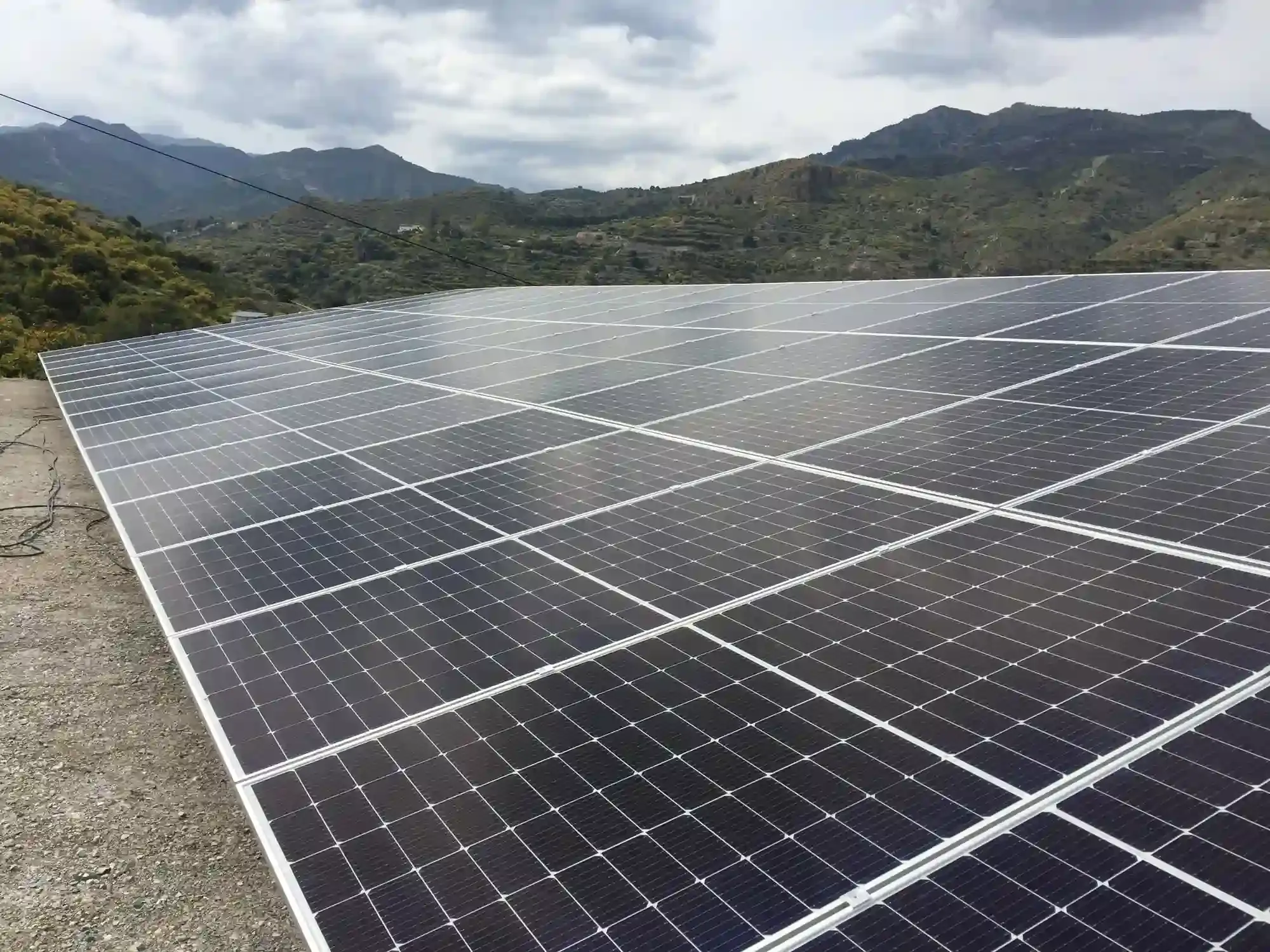 Paneles solares en un gran campo con montañas y cielo nublado al fondo.