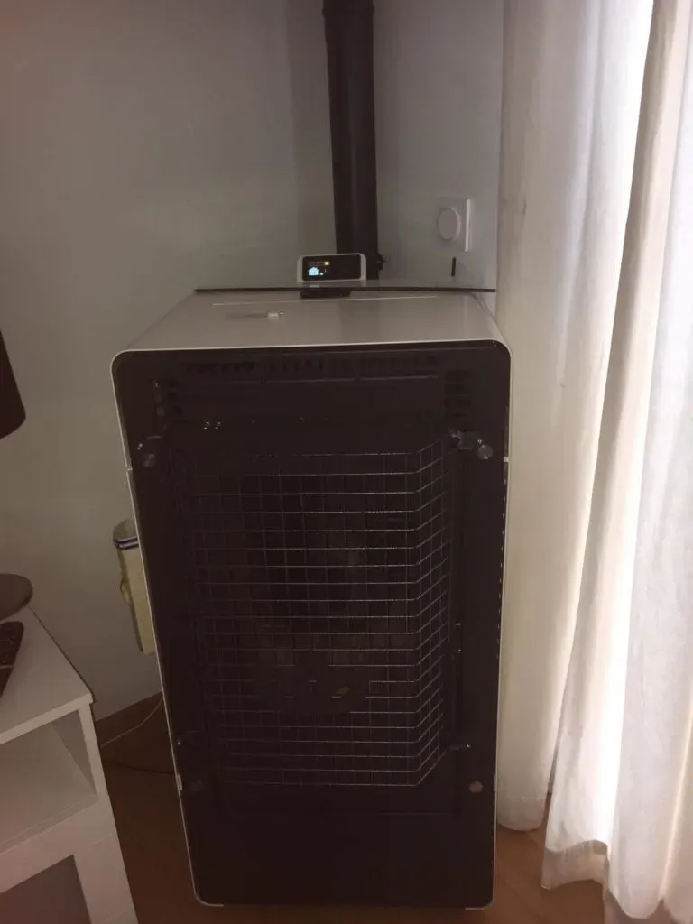 Aire acondicionado portátil negro junto a una ventana con cortinas blancas en la esquina de una habitación.